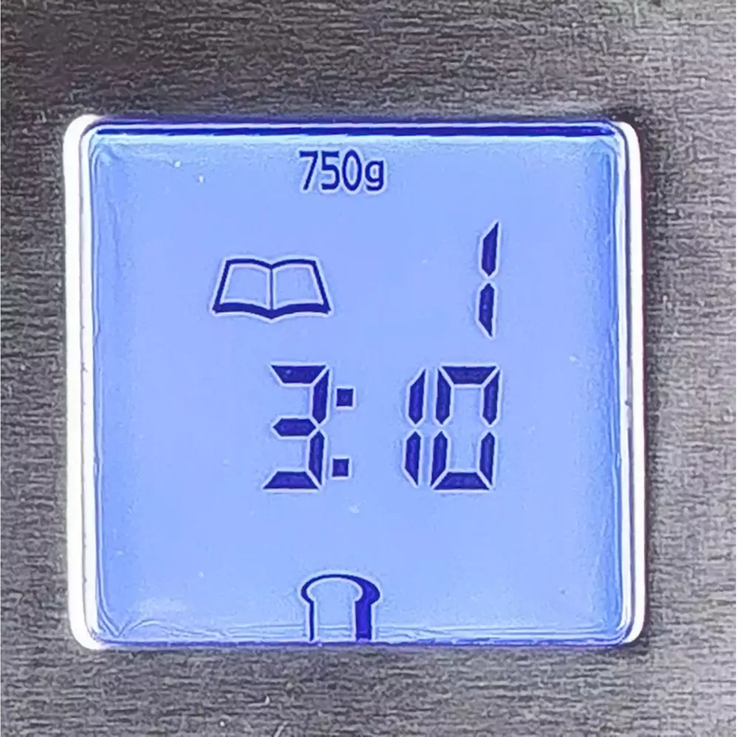 Blauw digitaal scherm met 750g, een boekpictogram, nummer 1 en 3:10. Er is ook een broodpictogram.