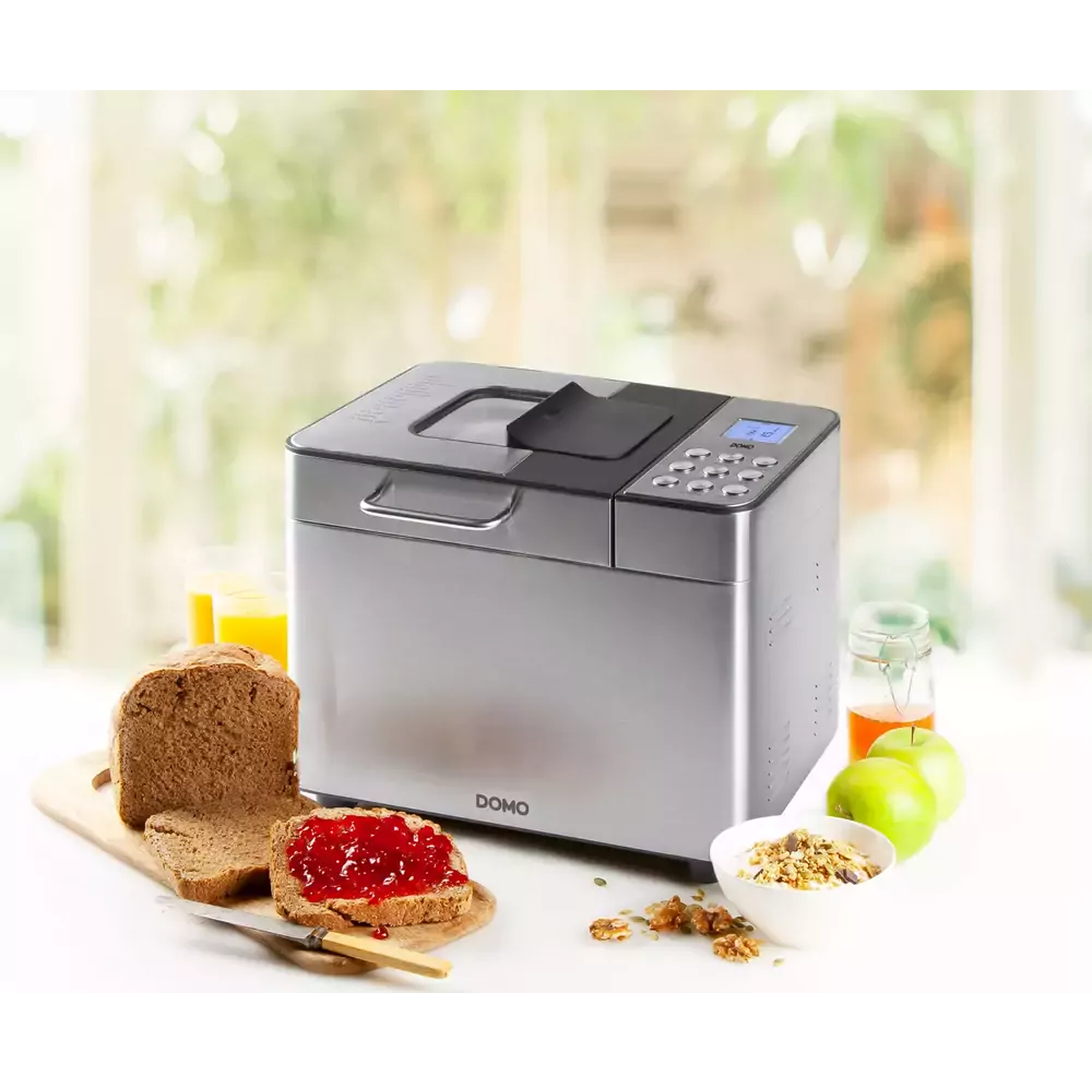 Een broodbakmachine naast sneetjes brood met jam. Ook een kom granola, appels en sap zijn in de scène.