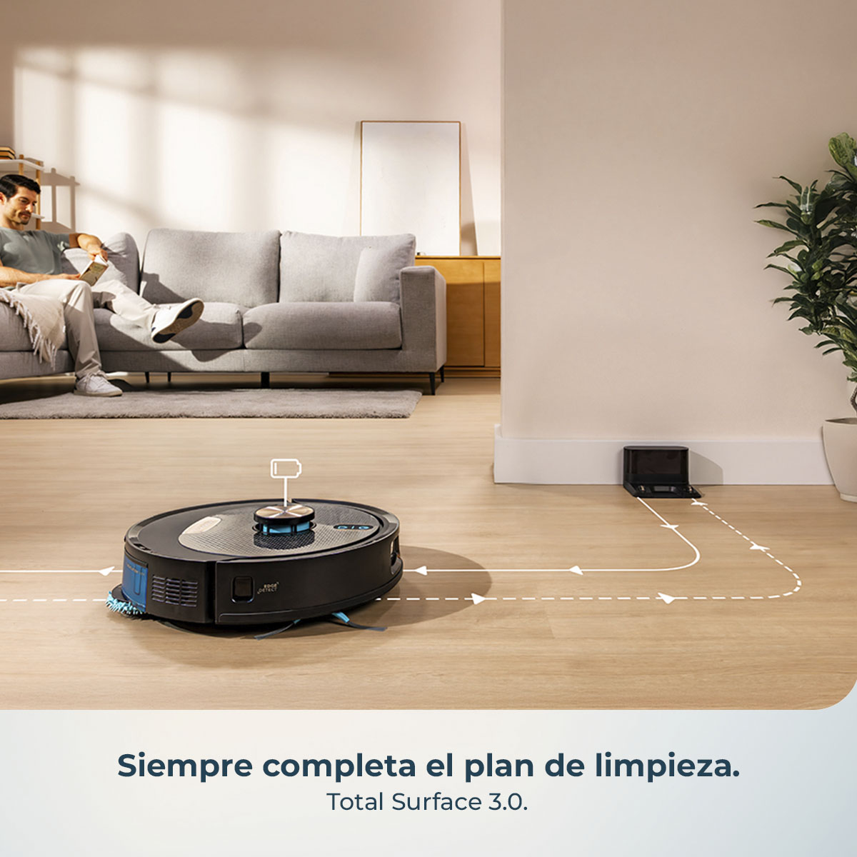 Una aspiradora robot limpia un suelo de madera. Un hombre está sentado en un sofá. Hay una planta en la esquina. El texto dice 'Total Surface 3.0'.