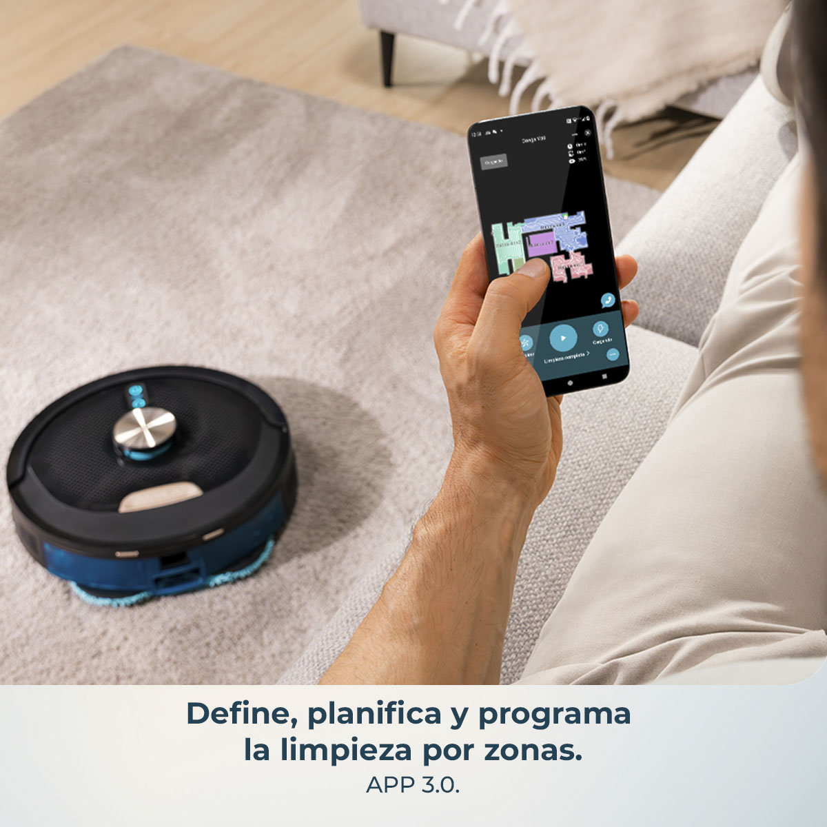 Una persona usa un teléfono para controlar un robot aspirador en una alfombra. El teléfono muestra un mapa de la habitación.