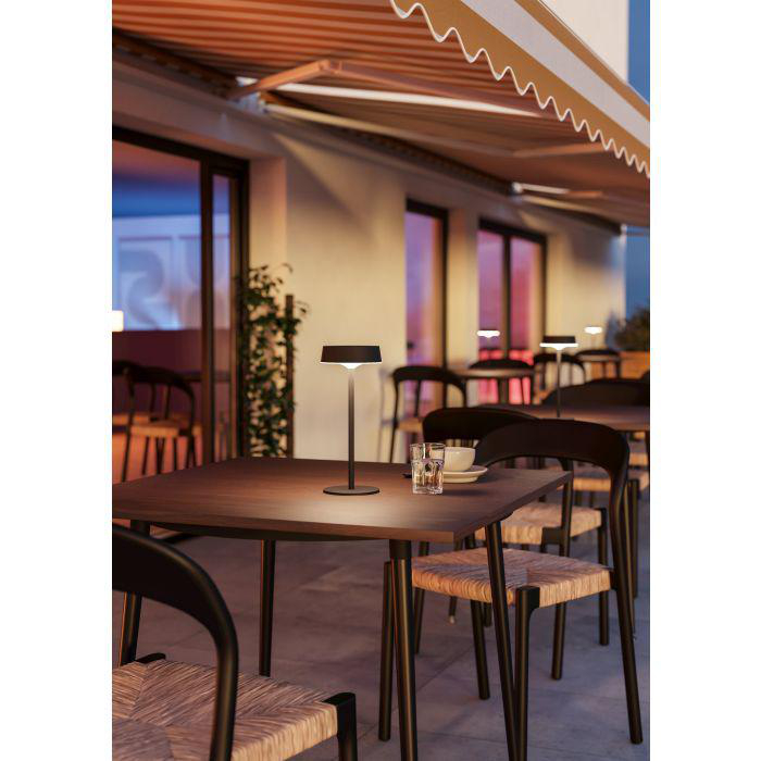 Restaurant im Freien. Tische mit Lampen, Stühlen und Gläsern. Markise. Abendlicht, warme Farben und Schatten.