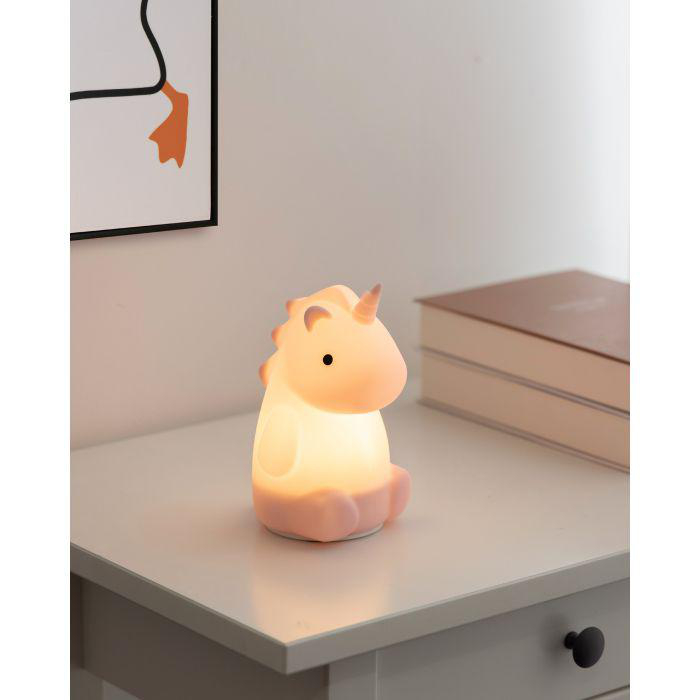 Eine leuchtende Einhornlampe steht auf einem weißen Tisch. Ein gerahmtes Bild und ein geschlossenes Buch sind im Hintergrund.
