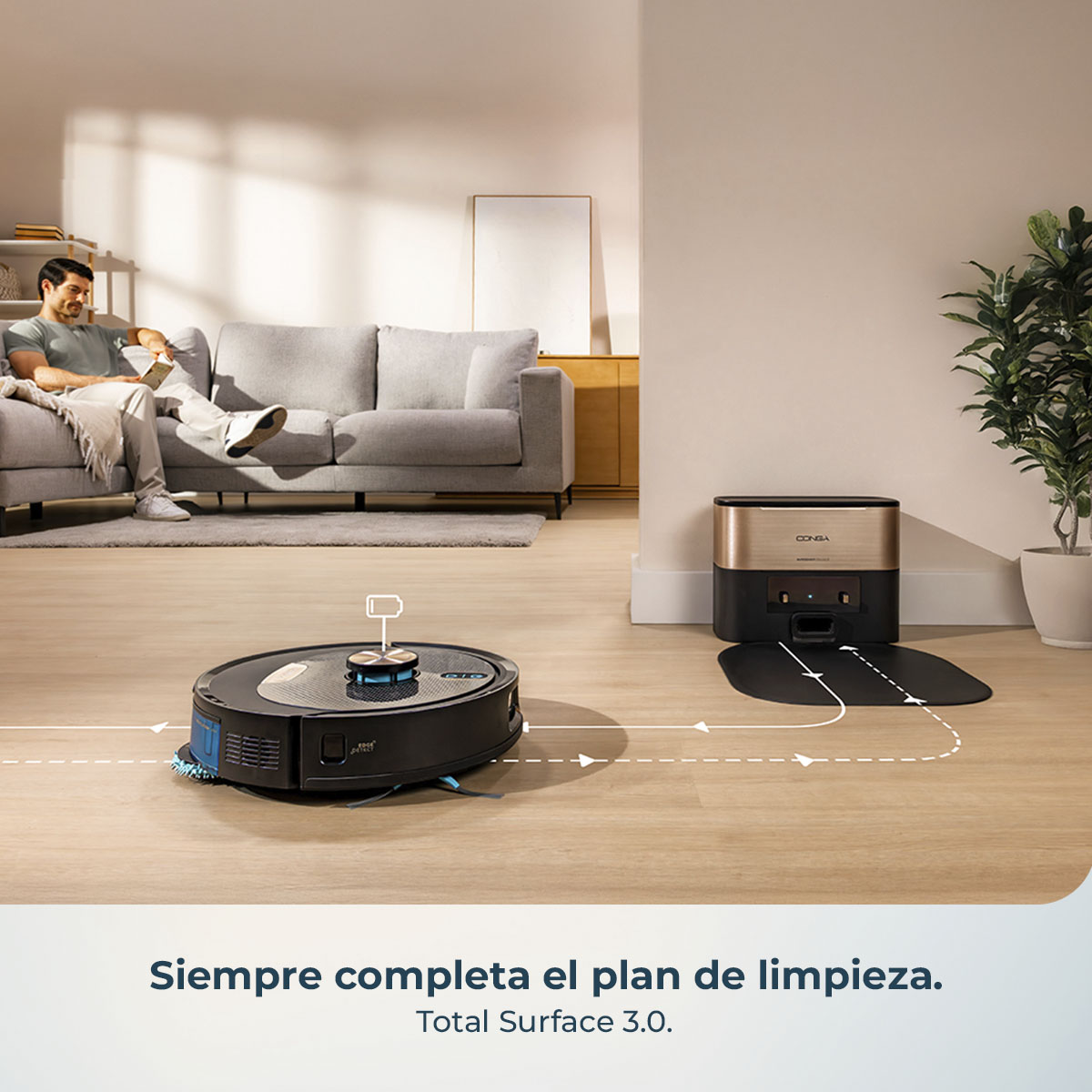 Un hombre se relaja en un sofá mientras una aspiradora robot limpia. Una estación de carga está cerca. El suelo es de madera.