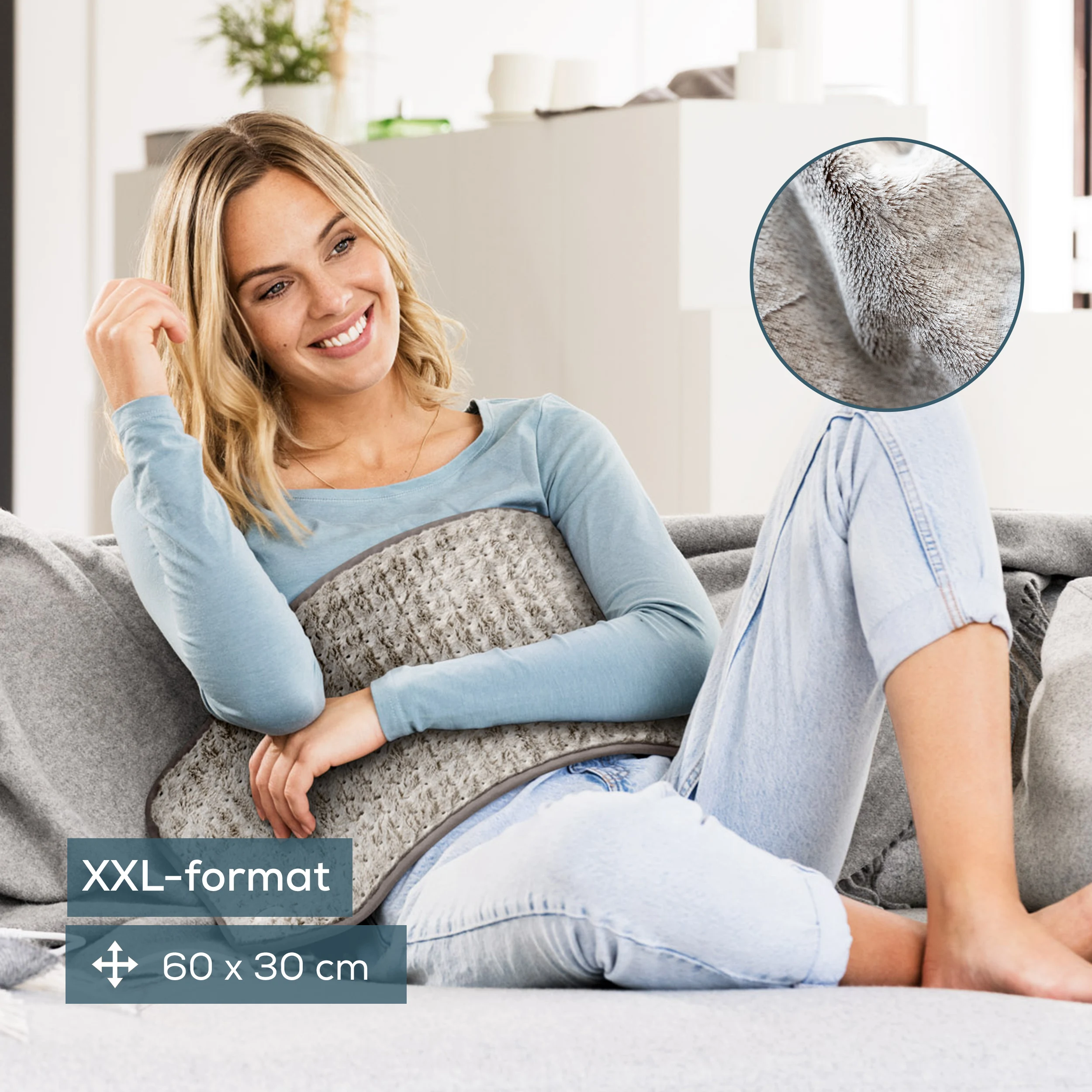 Donna su un divano con un termoforo. Indossa blu e jeans. Il termoforo è grigio.