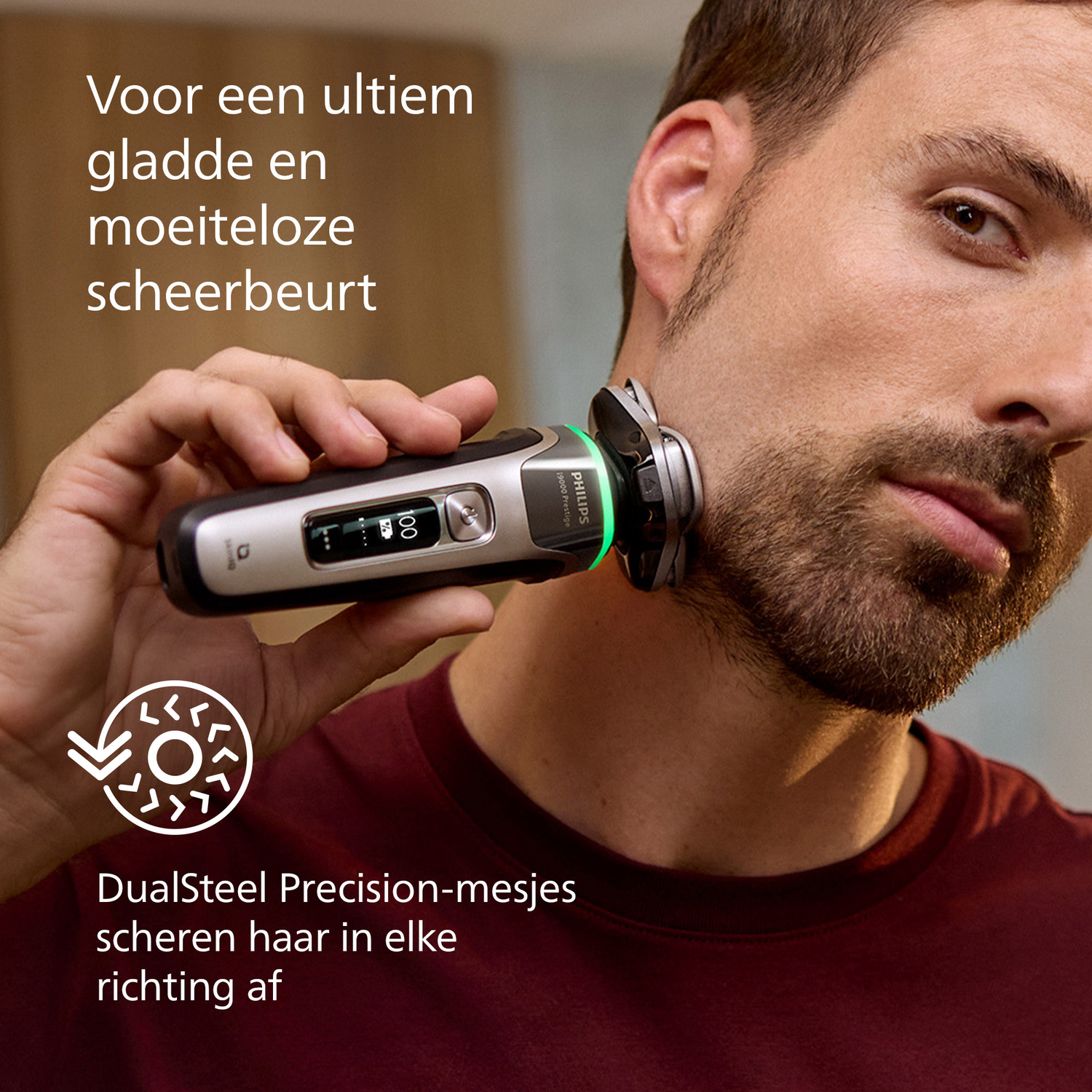 A man shaves his beard with an electric shaver. The shaver is silver and black. Text: 'DualSteel Precision-mesjes scheren haar in elke richting af'.