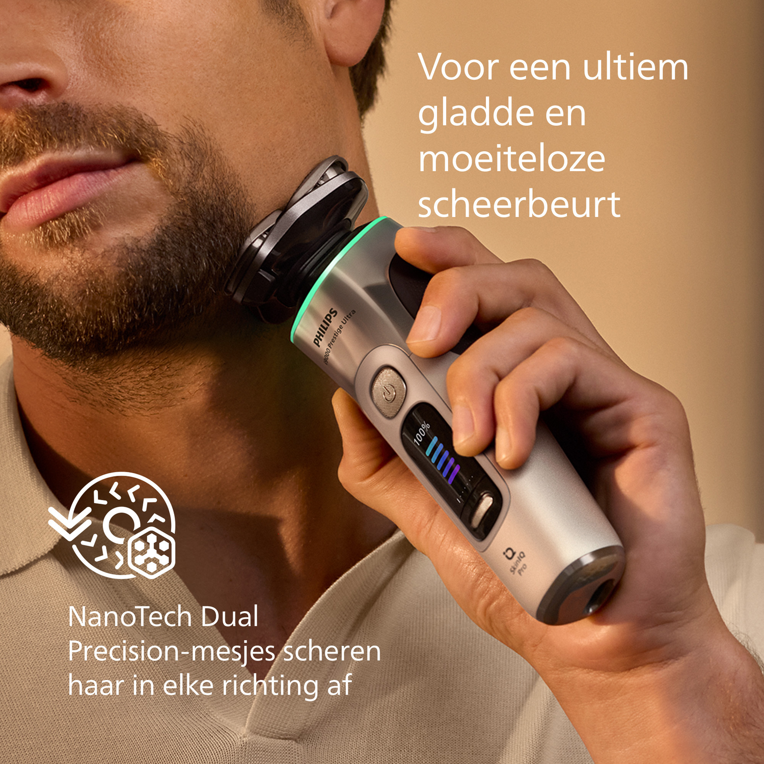 A man shaves his beard with an electric shaver. The shaver is silver and black, with a digital display showing 100% battery.