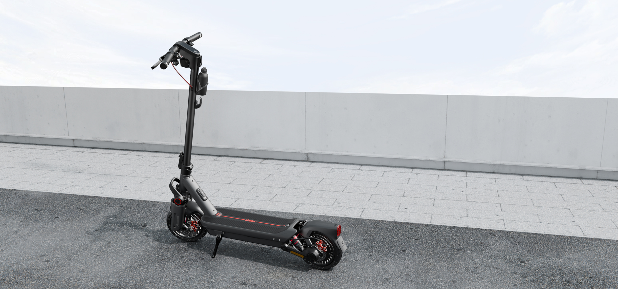 Egy fekete-szürke elektromos roller szürke járdán áll. A háttérben fehér fal és világoskék ég.