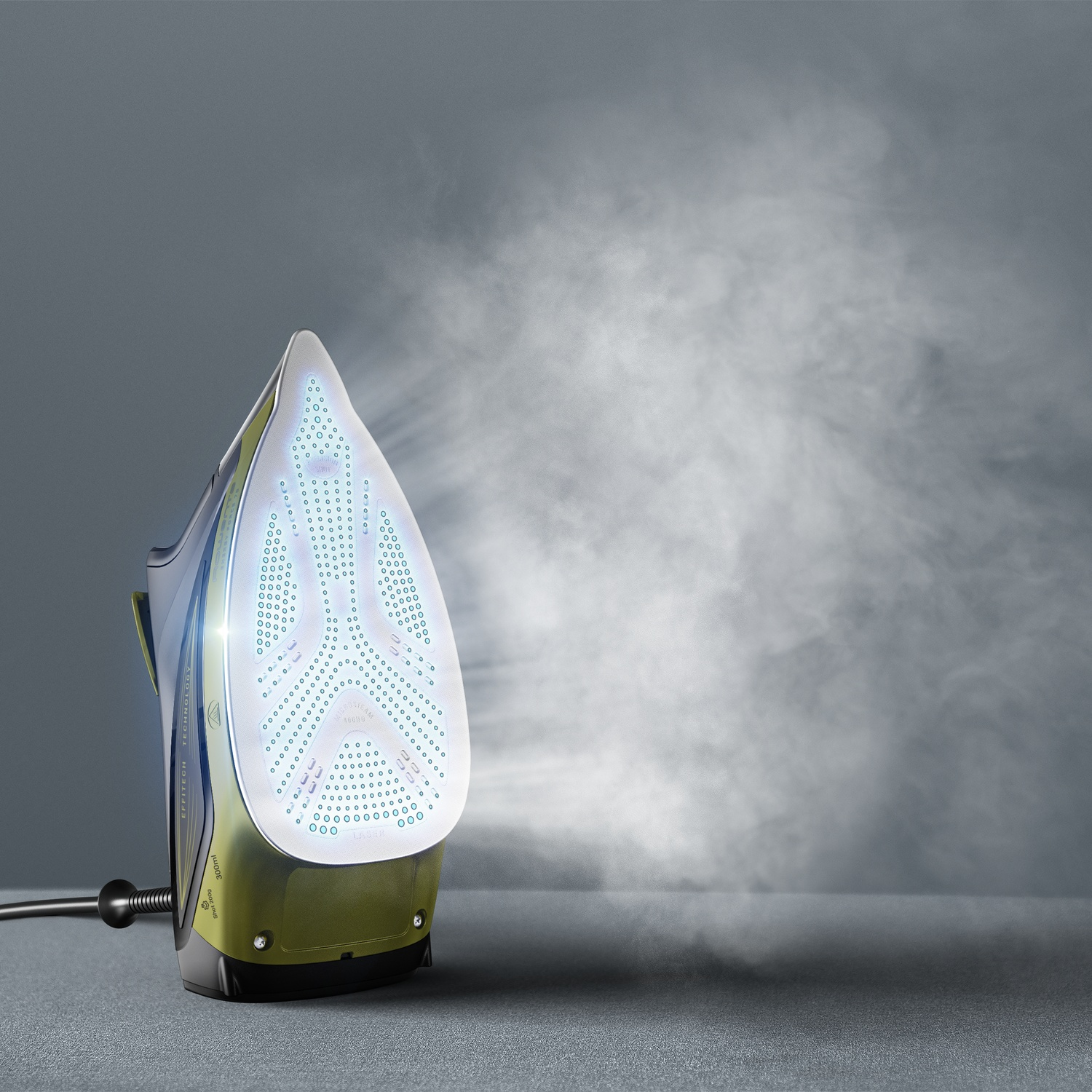 Un fer à repasser avec de la vapeur est sur une surface grise. Le fer est vert et gris avec une base blanche. La vapeur sort du fer.
