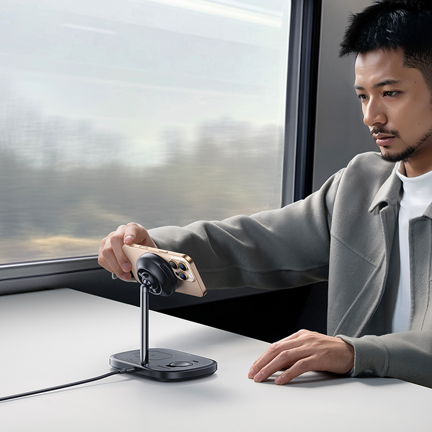 Un hombre sostiene un teléfono conectado a un soporte. Está en un tren, mirando el teléfono. El fondo está borroso.