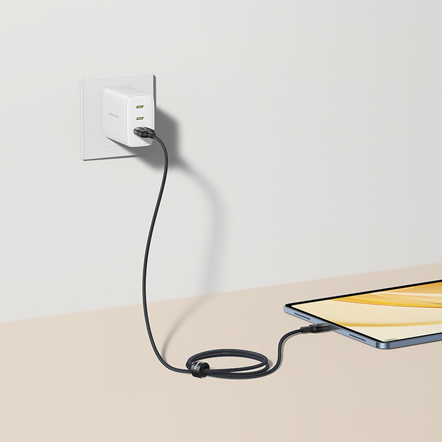 Un cargador blanco enchufado a la pared, conectado a una tableta con un cable negro. La tableta está sobre una superficie clara.