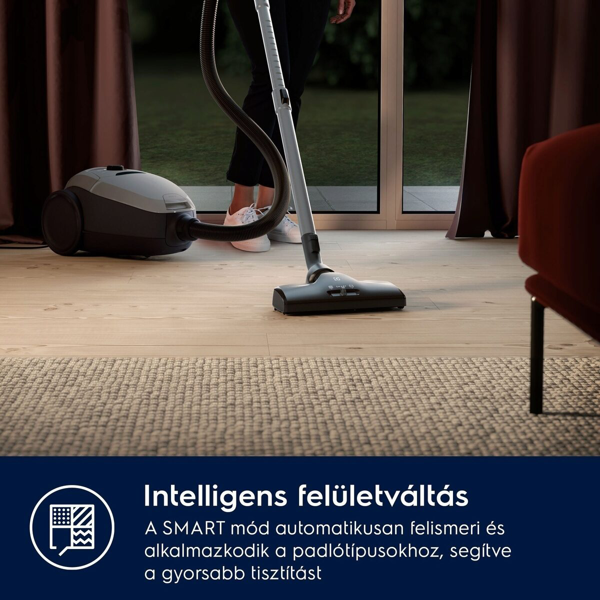 Egy személy porszívózza a fapadlót. Porszívó használatban. A háttérben egy szőnyeg és egy ablak látható.