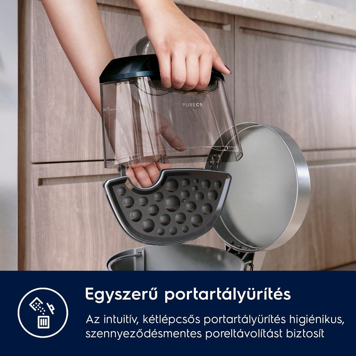 Egy személy egy átlátszó tartályt tart, fekete fedéllel és szürke alappal. A háttér egy fa szekrény.