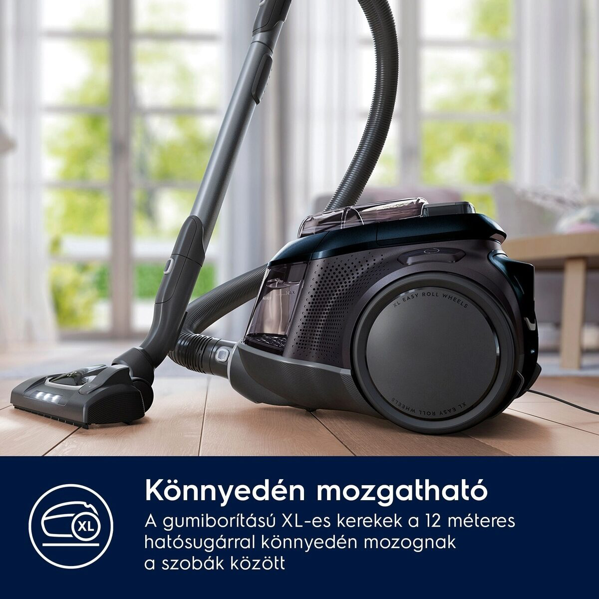 Egy fekete porszívó XL-es könnyen guruló kerekekkel egy fa padlón. Magyar szöveg alul.