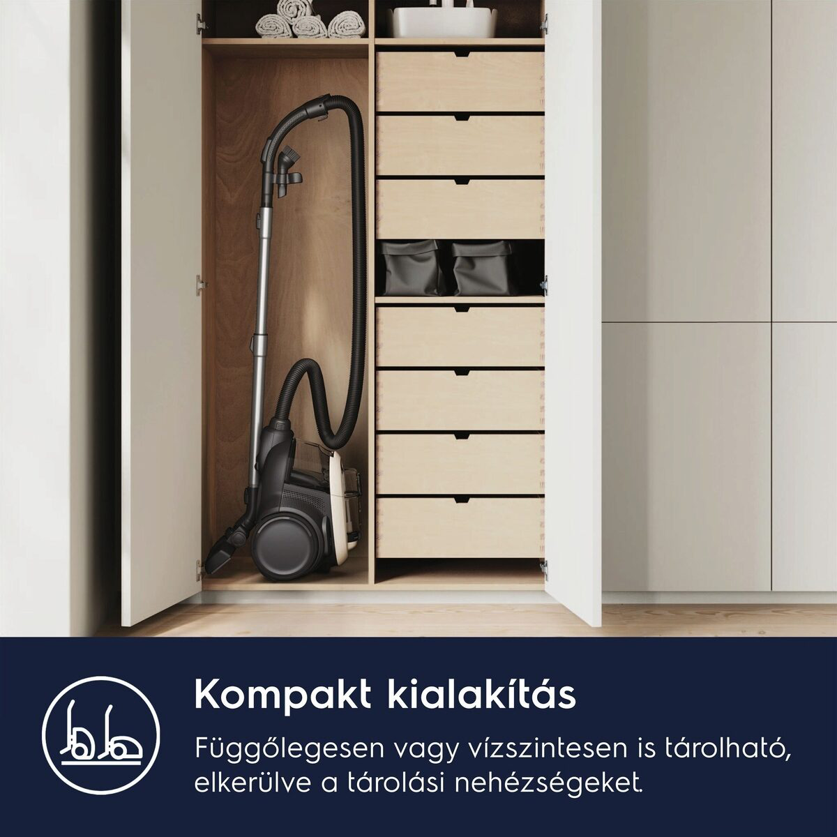 A porszívó egy fiókos szekrényben van tárolva. A szekrény világos fából készült. A porszívó fekete és ezüst.