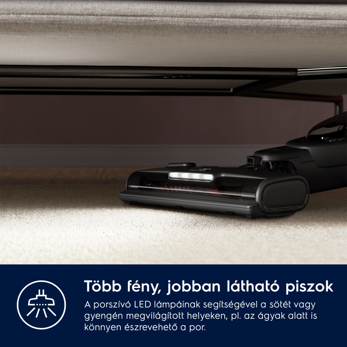 Egy fekete porszívó az ágy alatt, világítással, szőnyeget tisztít. A szöveg szerint: 'Több fény, jobban látható piszok'.