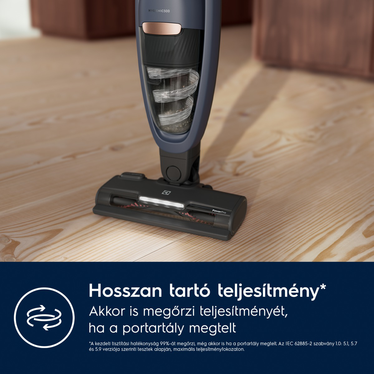 A porszívó közeli képe. Sötétkék, rózsaarany díszítéssel. A feje fekete, fa padlón van.
