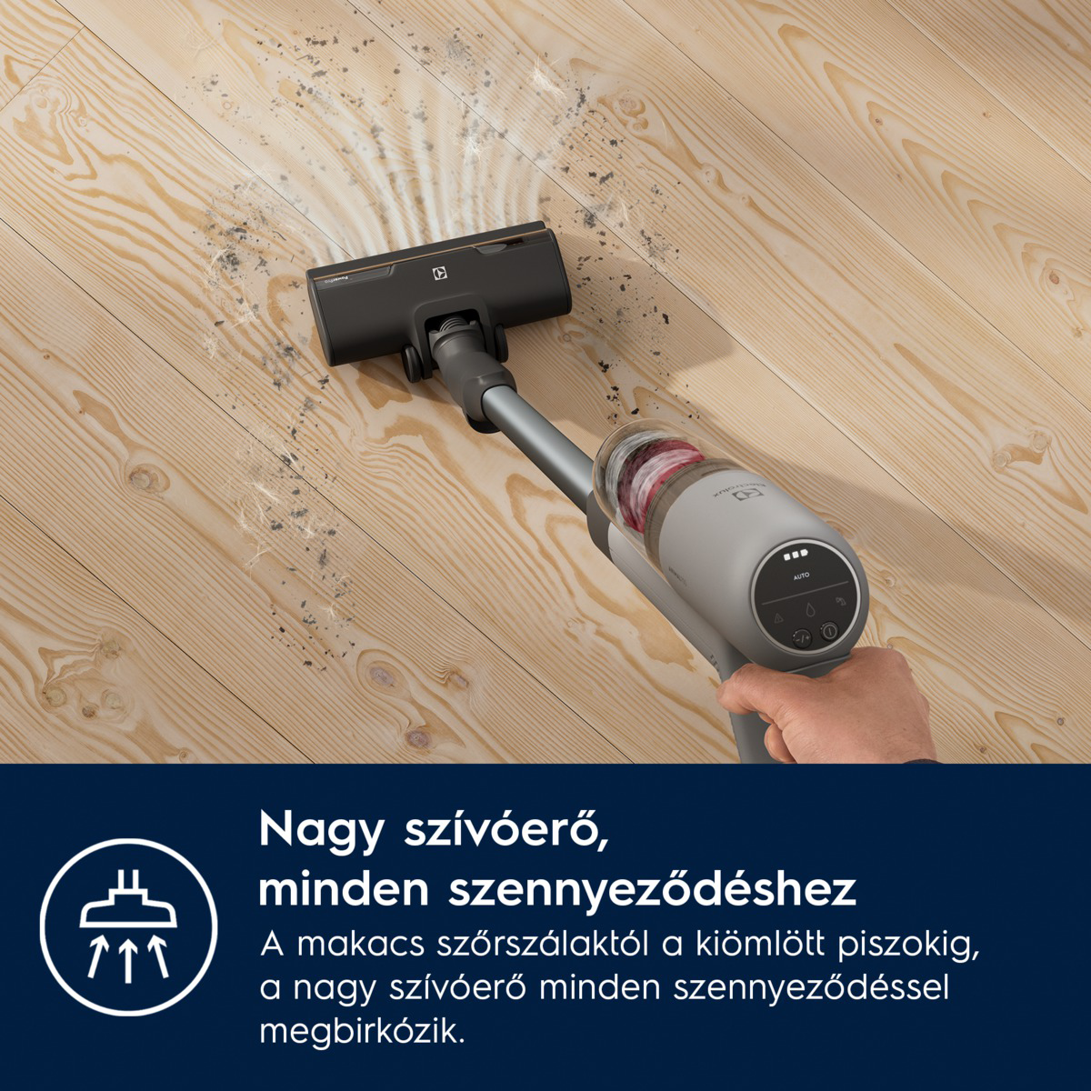 Egy szürke porszívó tisztít egy fapadlót. A porszívót egy kéz tartja. Por és törmelék látható a padlón.