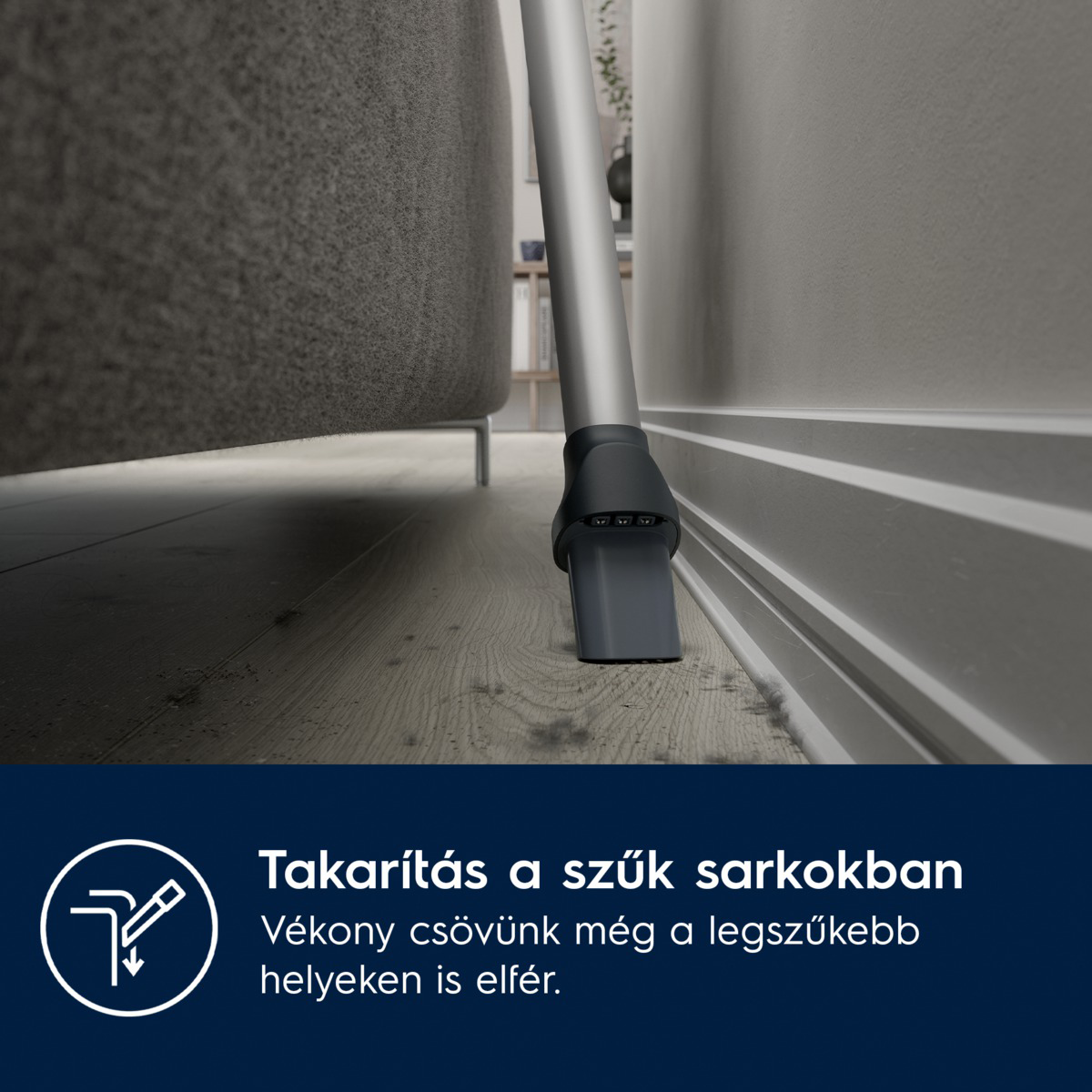 Egy porszívó tisztít egy sarkot. A fúvóka a fal és a kanapé közelében van. A padló fa.
