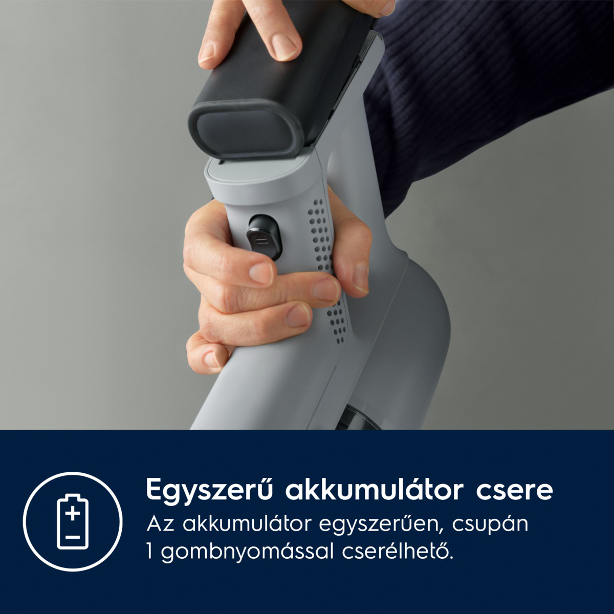 Kéz egy fekete akkumulátort cserél egy szürke porszívóban. A háttér egy egyszerű szürke.