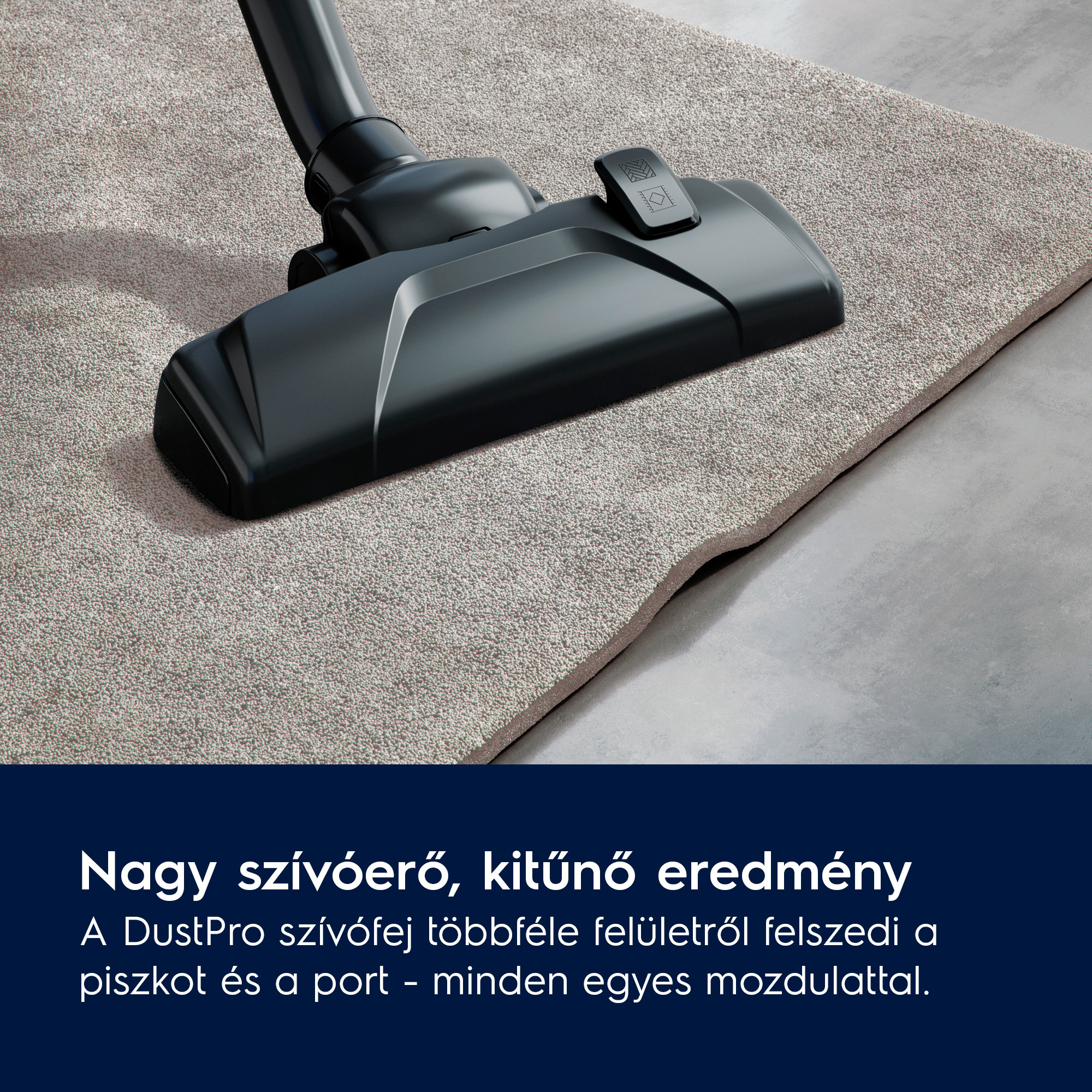 Egy fekete porszívófej egy bézs szőnyegen. A padló szürke. A porszívó szögben áll.