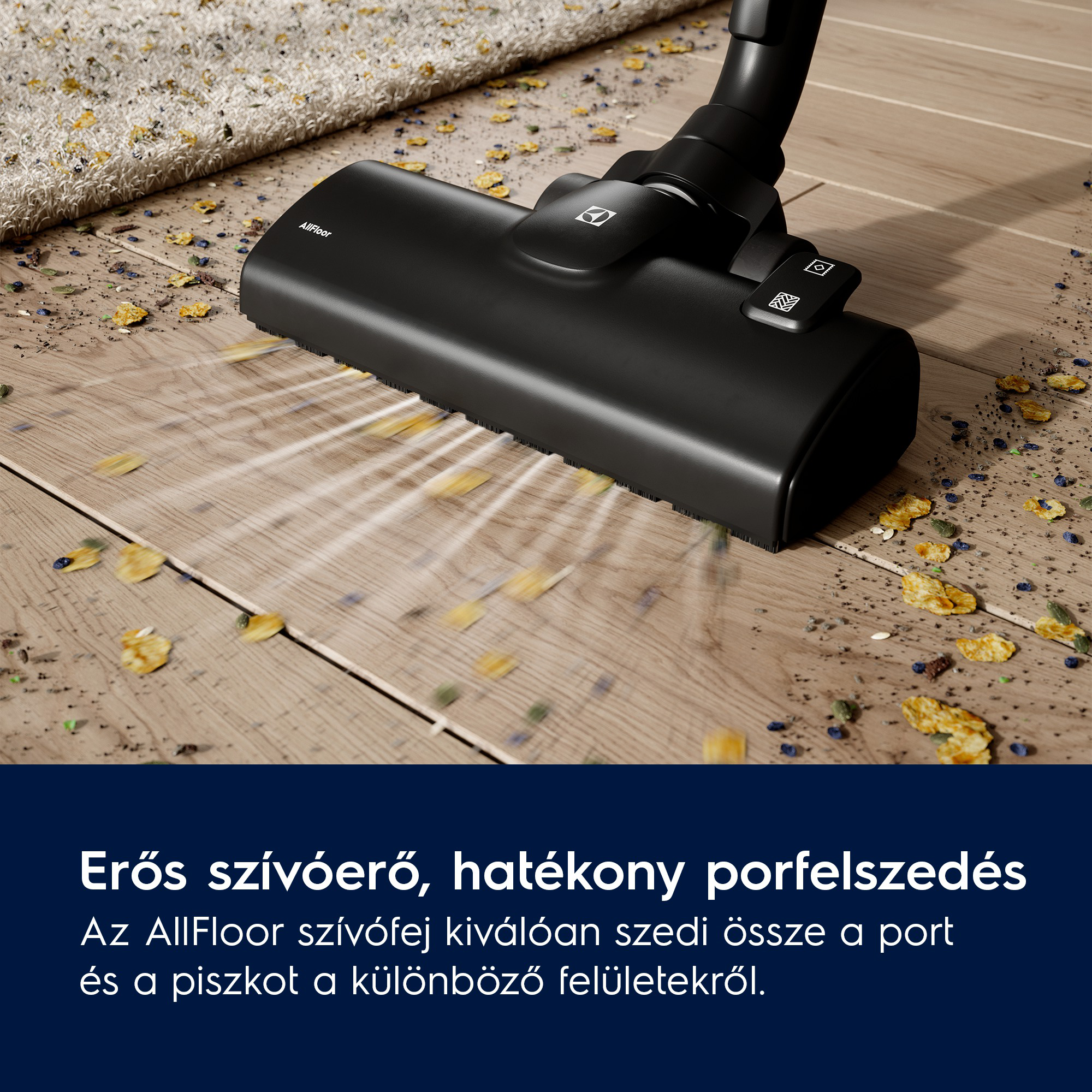 Egy fekete porszívófej a fa padlón. Törmelék, mint a levelek és az élelmiszer szétszórva. Egy szőnyeg részben látható.