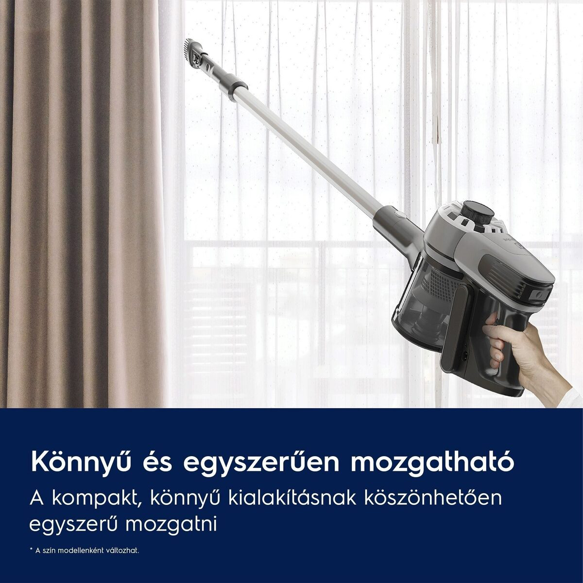 Egy kéz egy szürke-fekete akkus porszívót tart, egy áttetsző fehér függöny felé mutatva, balra barna függönnyel.