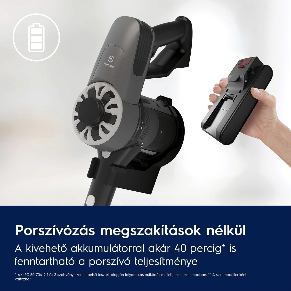 Egy szürke Electrolux porszívó látható, kivehető akkumulátorral, egy kézzel, amely egy külön akkumulátort tart.