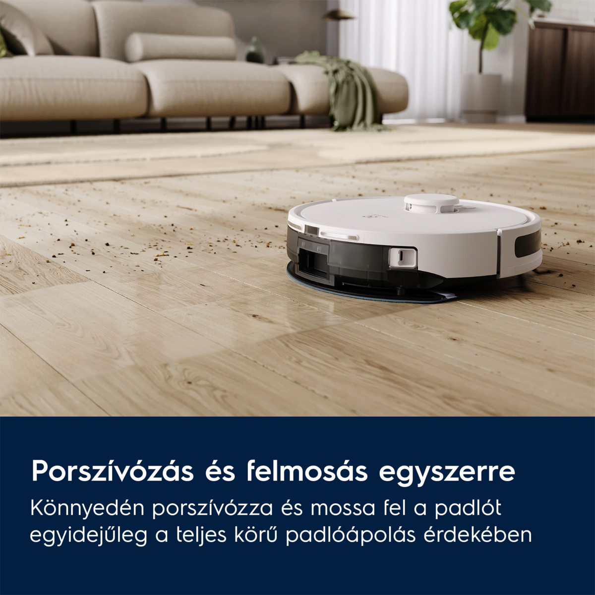 Egy robotporszívó tisztít egy fapadlót. Háttérben egy kanapé és növények láthatók.