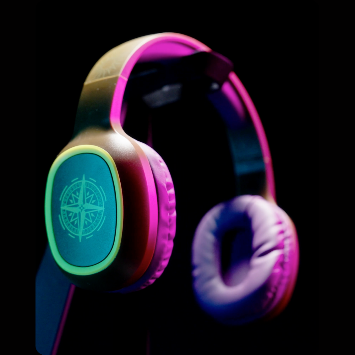 Słuchawki z turkusowymi akcentami, logo róży wiatrów i różowo-fioletowym oświetleniem na czarnym tle.