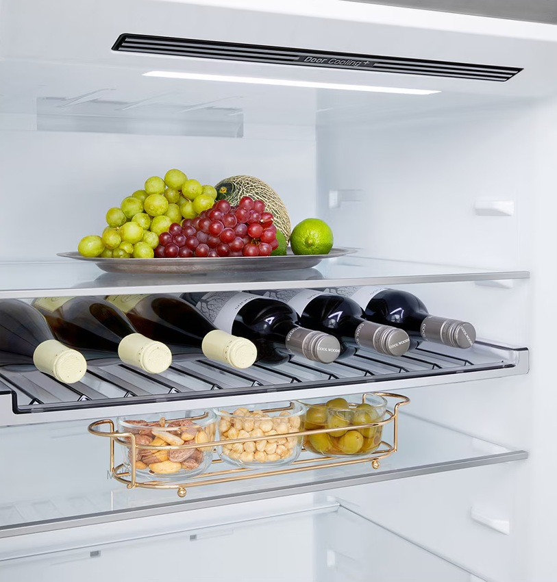 W lodówce: winogrona, melon, limonka na tacy. Butelki wina poniżej. Orzechy i oliwki w szklanych miskach.