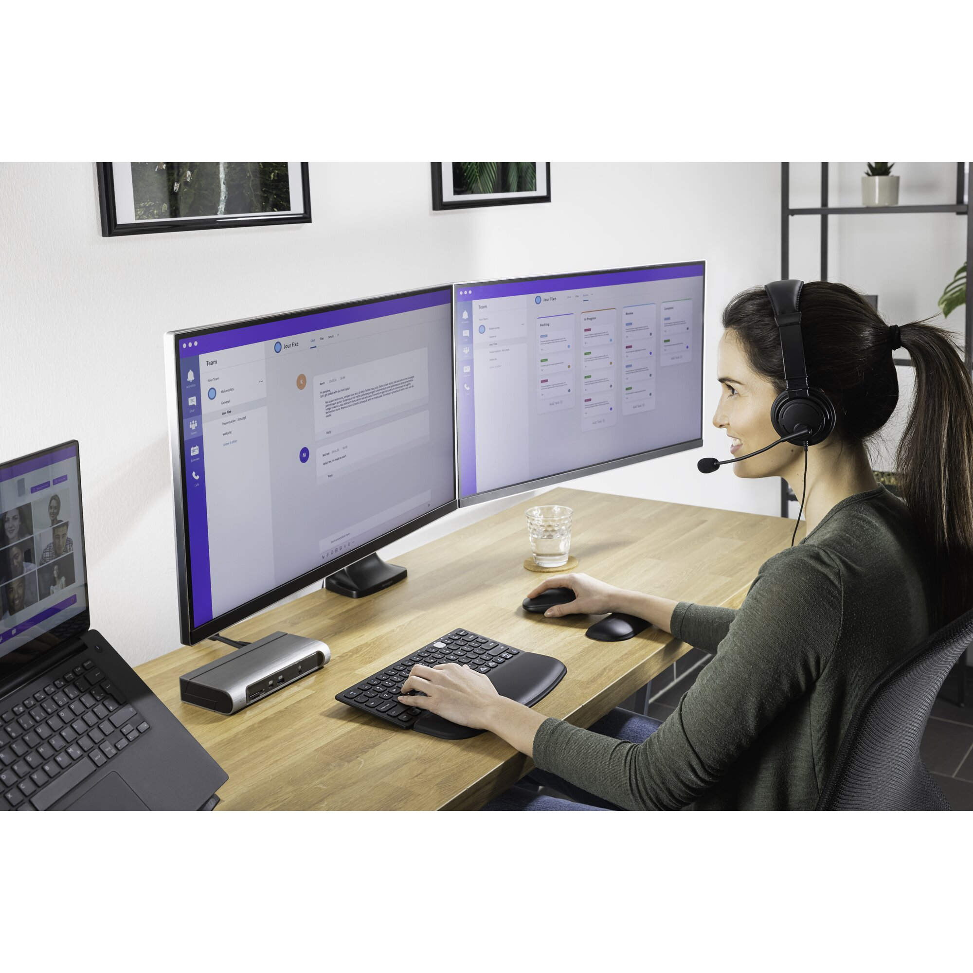 Frau mit Headset arbeitet an einem Computer mit zwei Bildschirmen, Tastatur und Maus. Ein Laptop ist ebenfalls vorhanden.