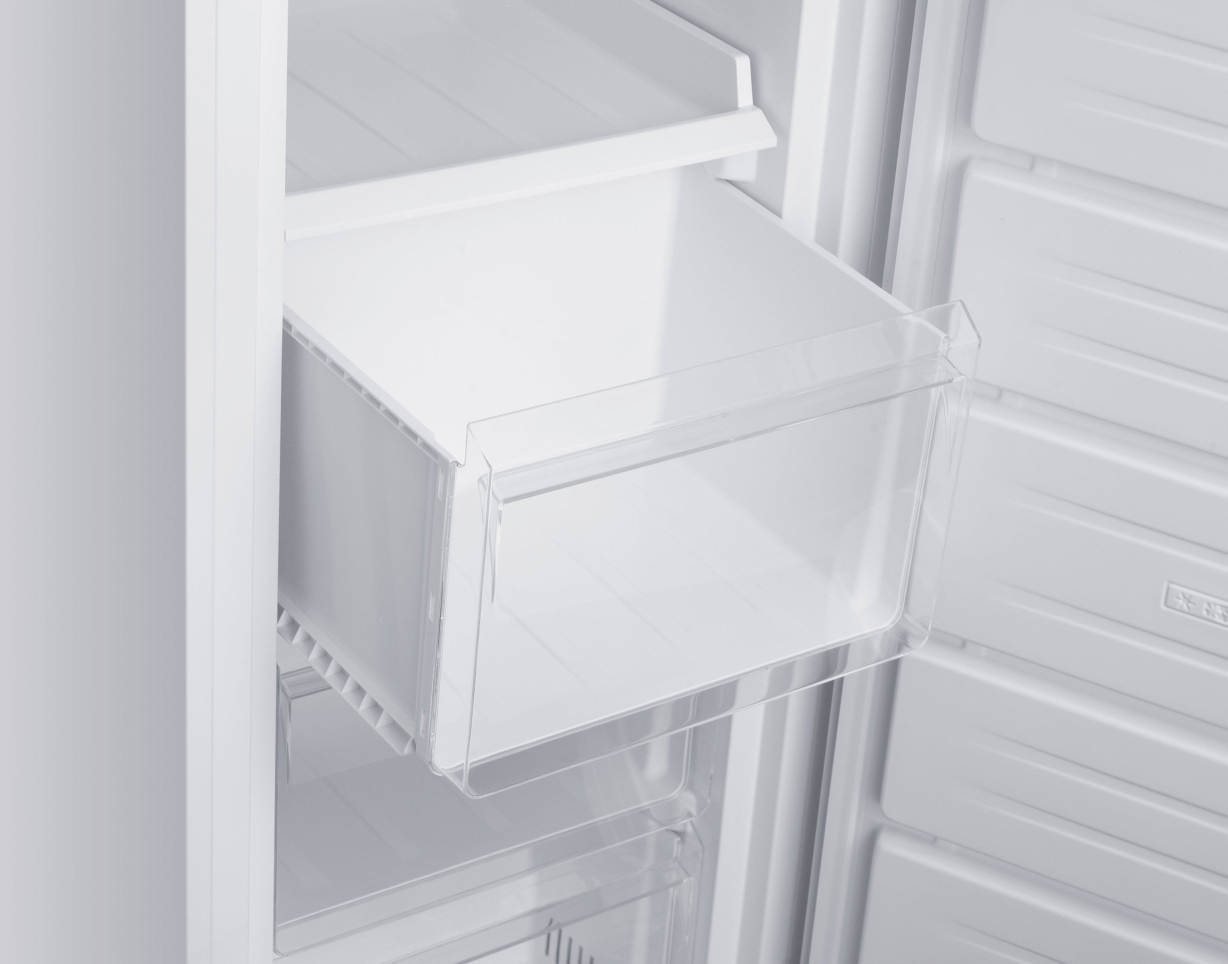 À l'intérieur d'un réfrigérateur blanc, un tiroir transparent est sorti. D'autres compartiments blancs sont visibles.