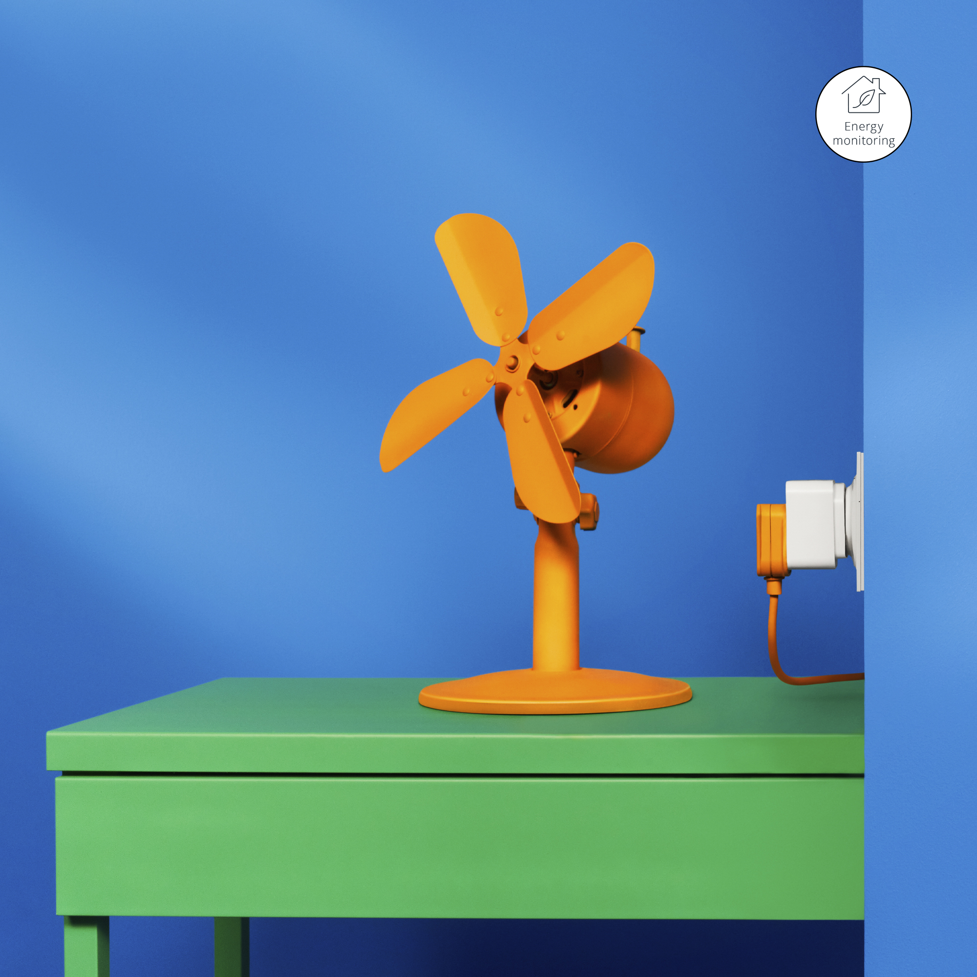 Ein orangefarbener Ventilator auf einem grünen Tisch mit blauem Hintergrund. Ein Stecker ist an der Wand angeschlossen.