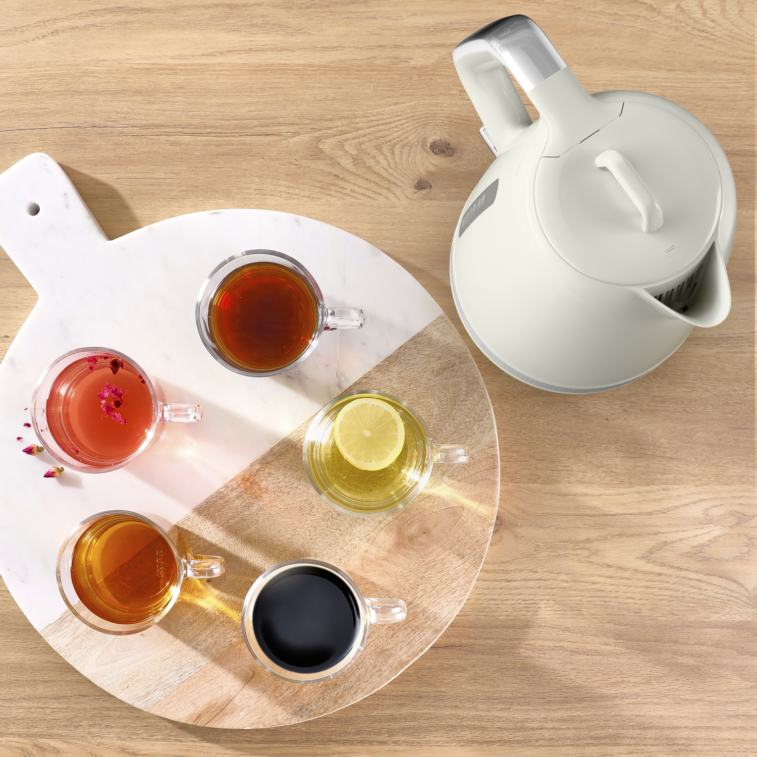 Overhead shot of a wooden table with a white kettle and a marble and wooden tray with four glass cups of tea.
