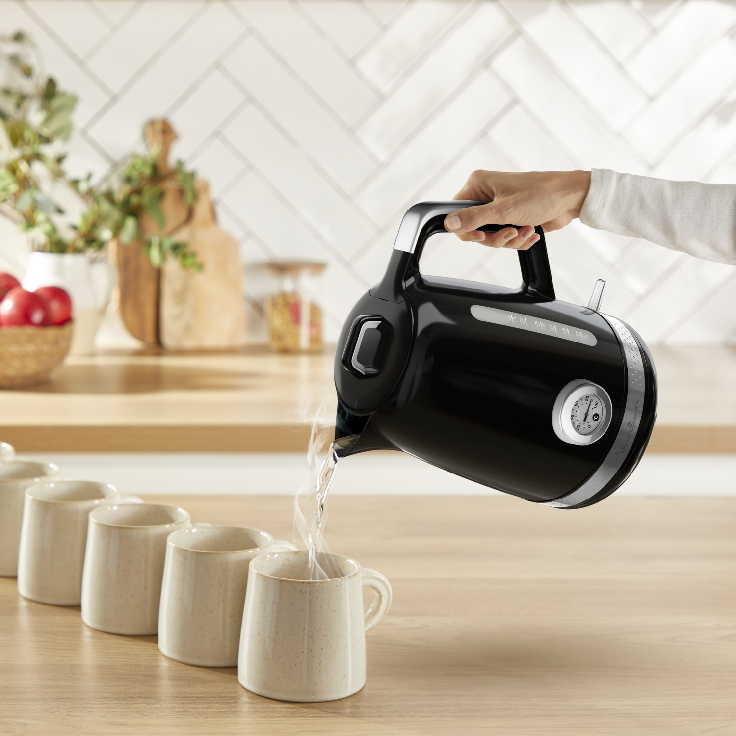 Une bouilloire noire verse de l'eau chaude dans une tasse. D'autres tasses sont alignées sur une surface en bois.