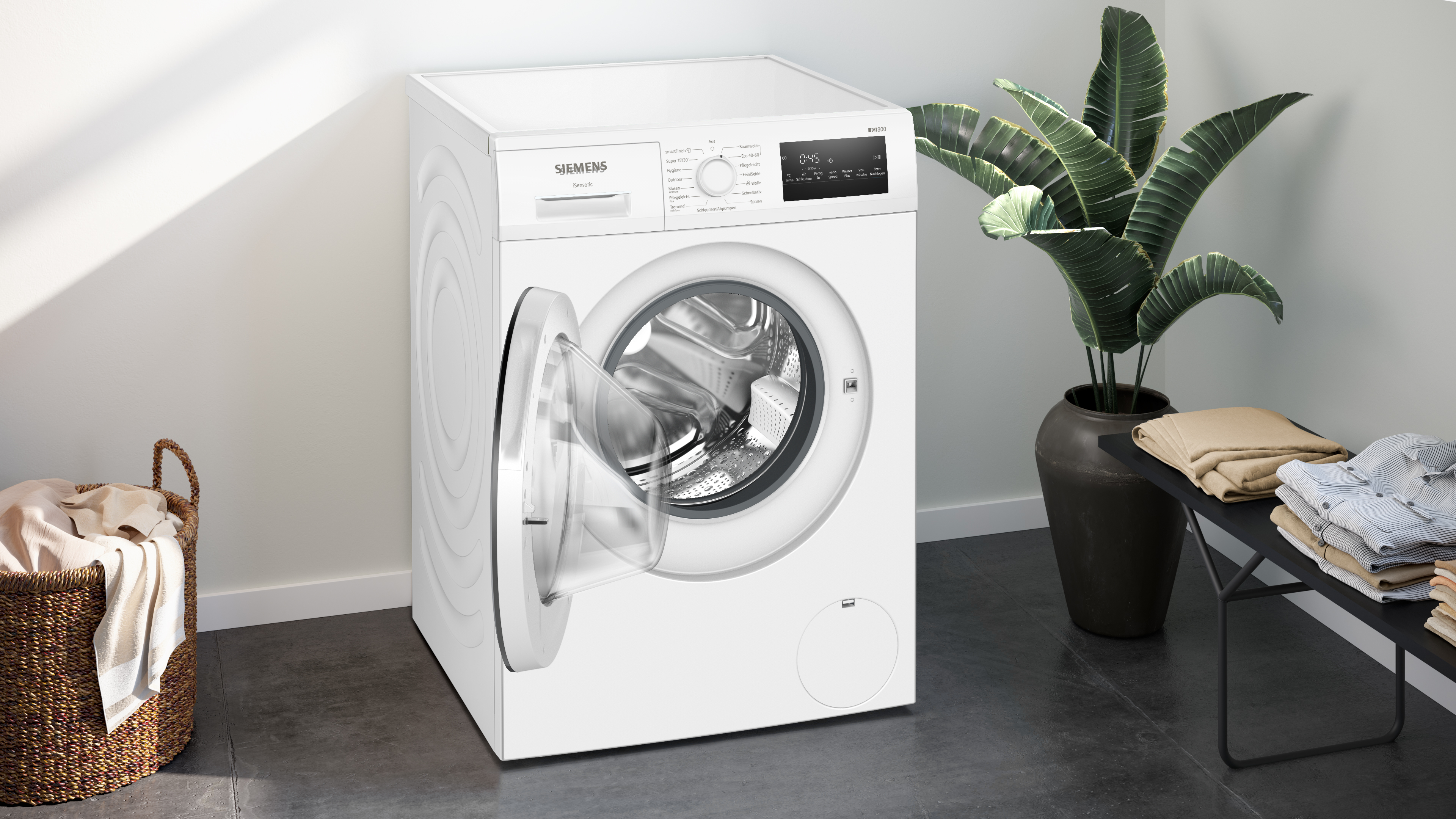 Eine weiße Siemens-Waschmaschine mit offener Tür. Ein Wäschekorb und eine Pflanze sind in der Nähe.