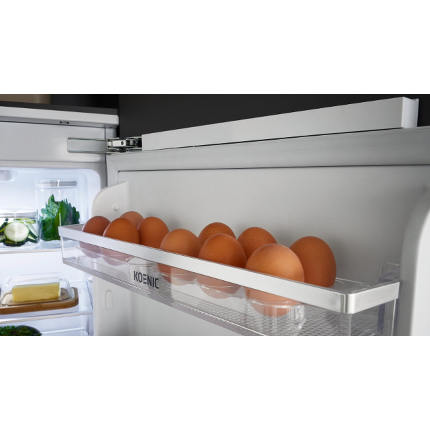À l'intérieur d'un réfrigérateur, une étagère contient des œufs bruns. Du beurre sur une planche en bois et des légumes sont également visibles.