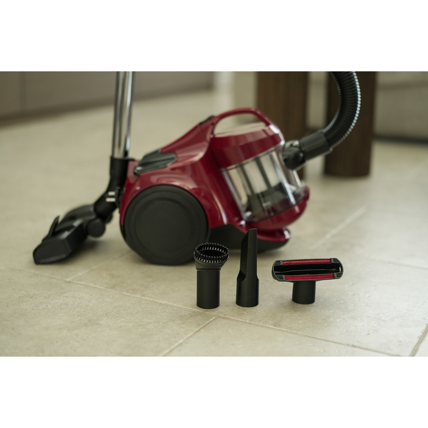 A red vacuum cleaner with accessories on a tiled floor. Three black attachments are in front of the vacuum cleaner.