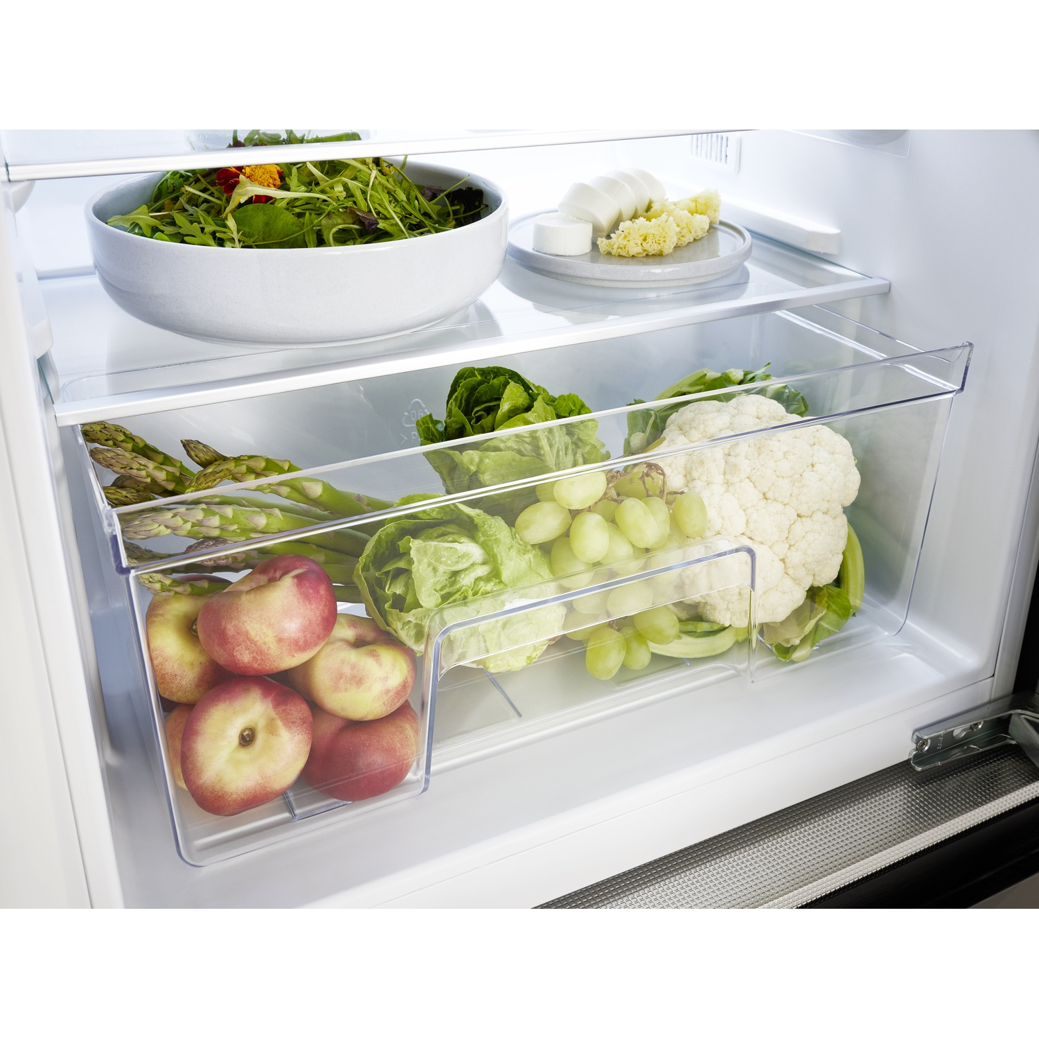 Inside a refrigerator, salad, cheese, cauliflower, grapes, peaches, and asparagus are visible.