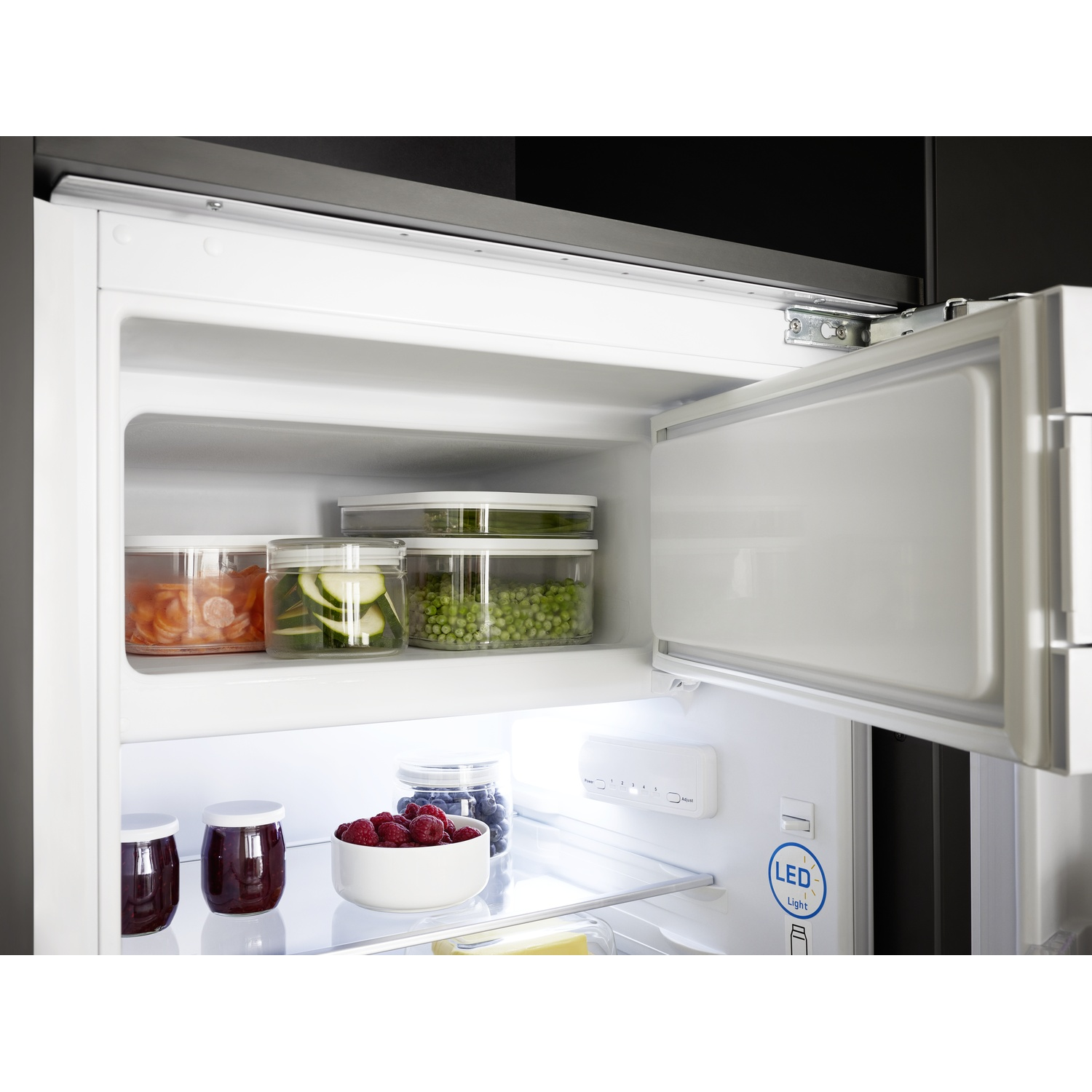 Open refrigerator with food containers. Jars of jam, berries, and vegetables are visible. LED light is on.