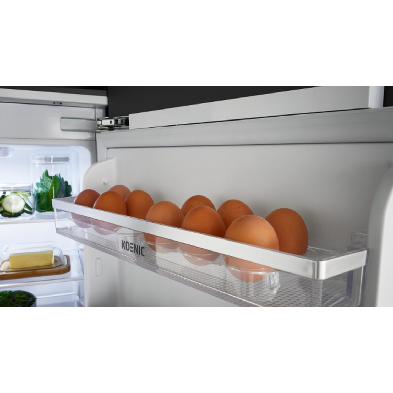 Inside a refrigerator, a transparent egg tray holds several brown eggs. Other shelves show vegetables and butter.