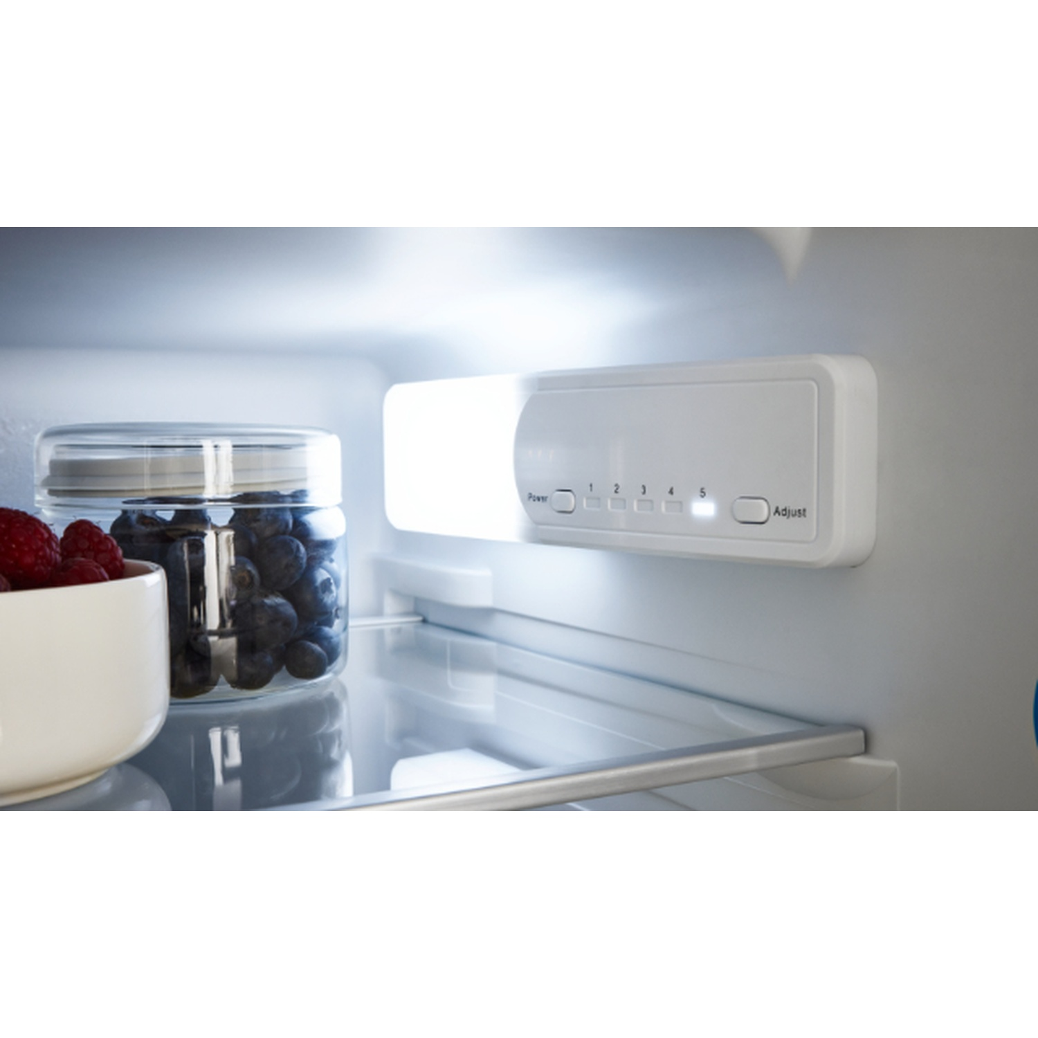 À l'intérieur d'un réfrigérateur : myrtilles dans un bocal, framboises dans un bol, luminaire blanc avec réglages et une étagère.