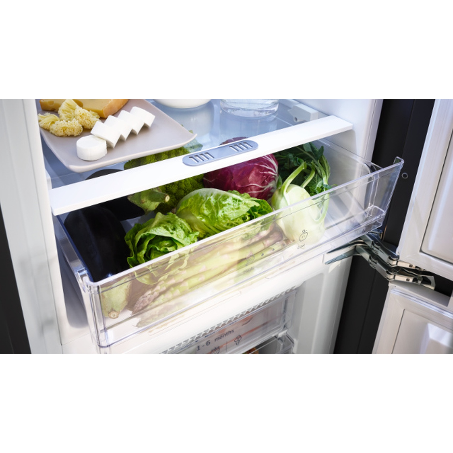 Open refrigerator with vegetables in a drawer, cheese and snacks on top shelf. Lettuce, cabbage, asparagus are visible.