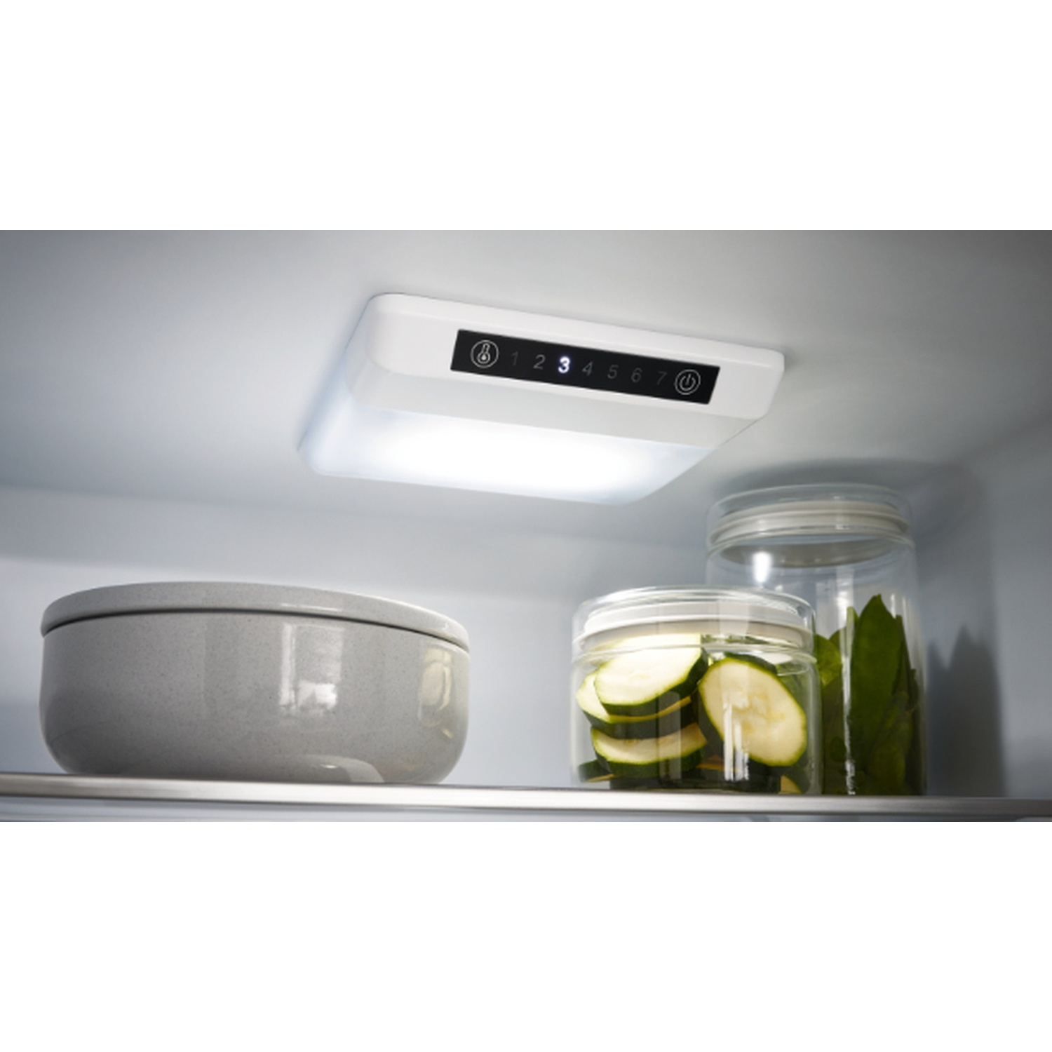 Inside a fridge: a white light, a gray bowl, jars of zucchini and leaves. Digital display shows numbers.