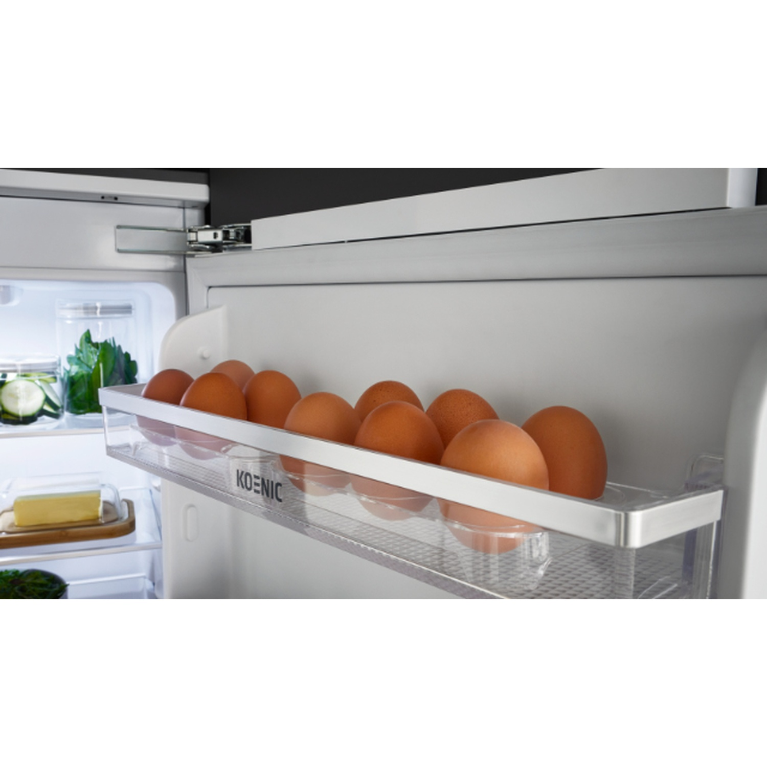 Inside a fridge, a clear egg holder contains brown eggs. Other items like butter, vegetables, are visible. The fridge is open.