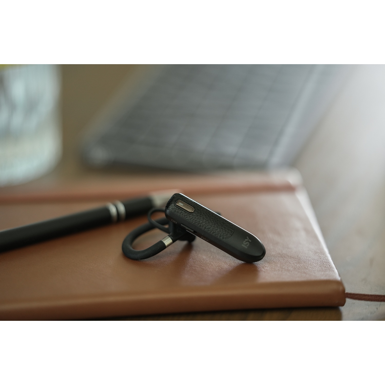 A black headset rests on a brown leather notebook, with a black pen beside it. A blurry background shows a keyboard.