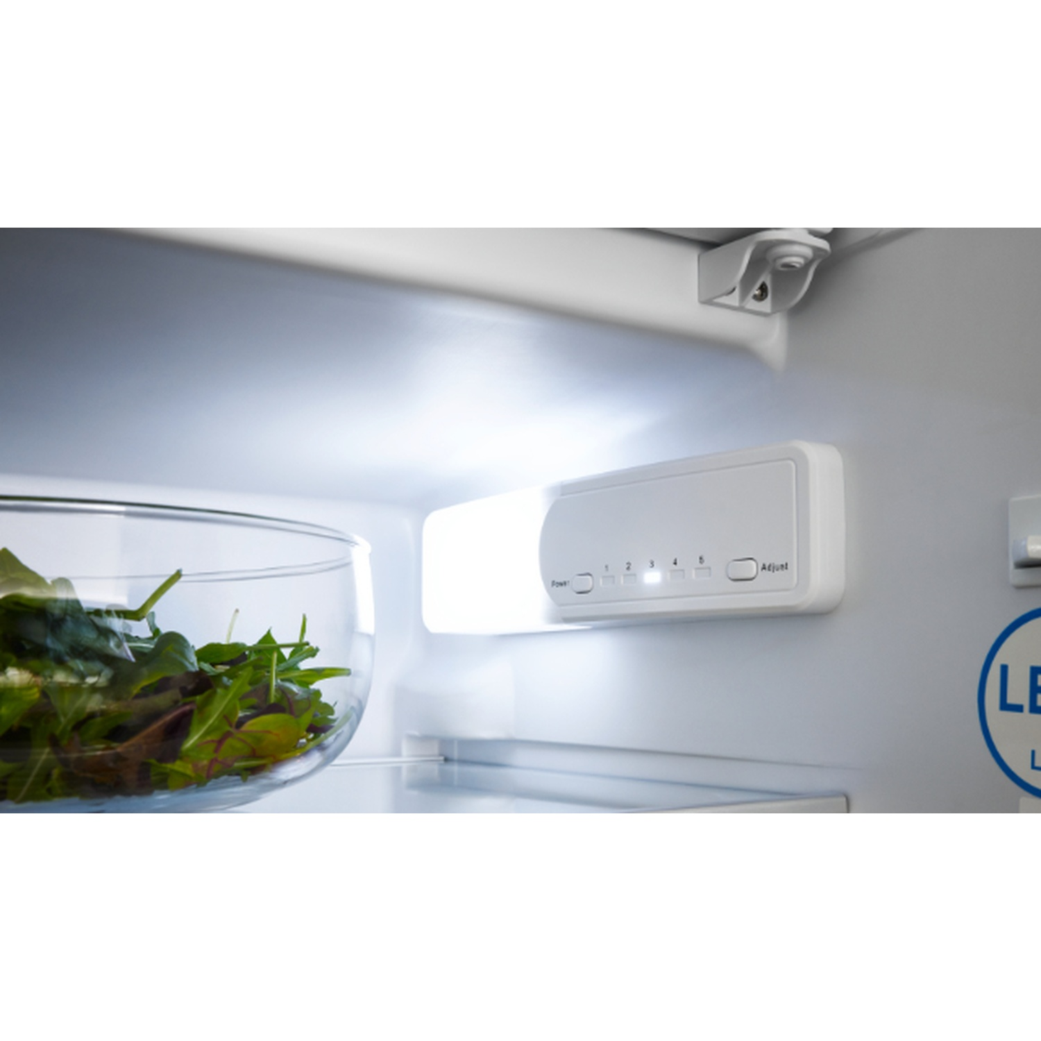 À l'intérieur d'un réfrigérateur : salade dans un saladier en verre, lumière vive, panneau de contrôle avec réglages et autocollant LED.