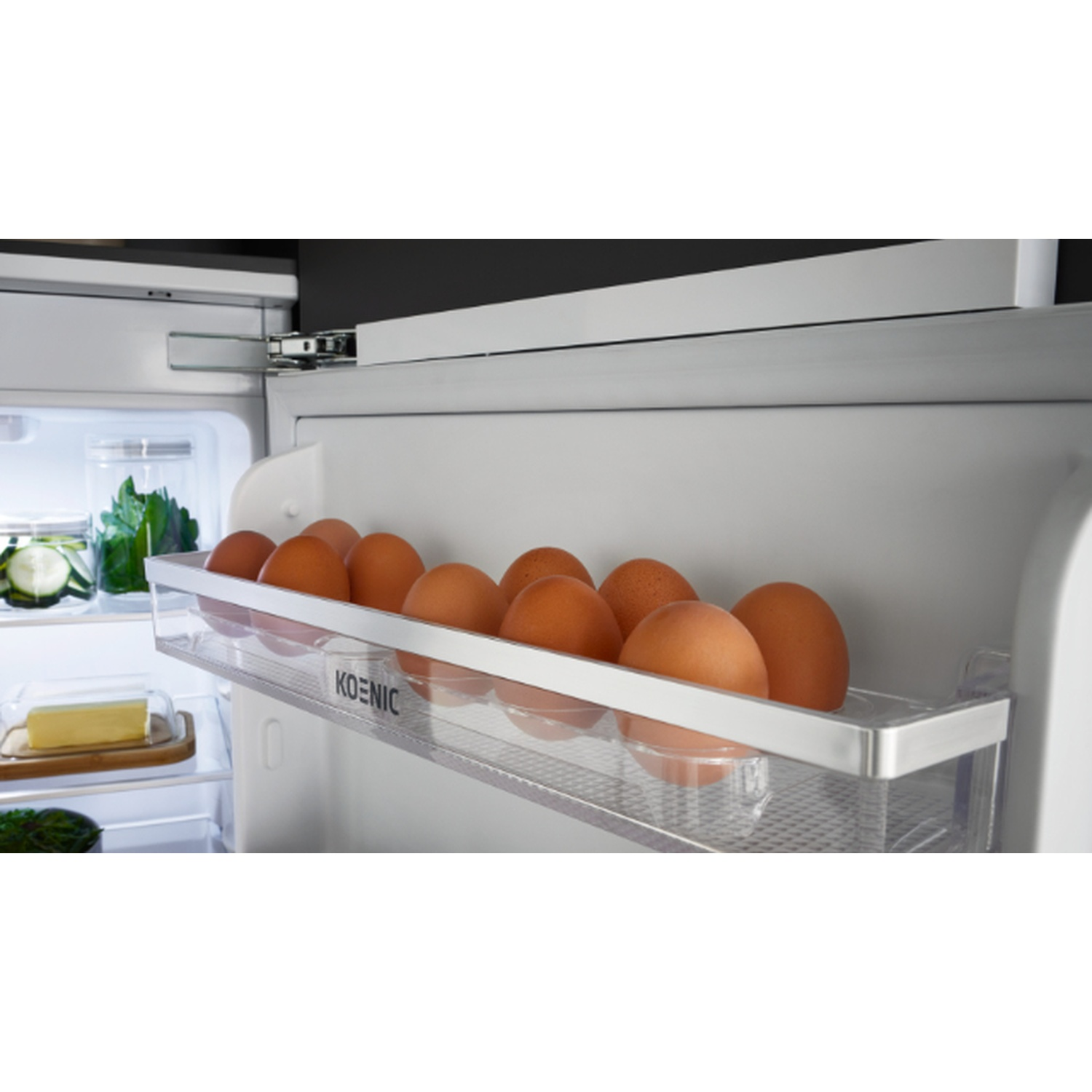 À l'intérieur d'un réfrigérateur, une étagère contient des œufs bruns. D'autres étagères contiennent des légumes et du beurre. La porte est ouverte.