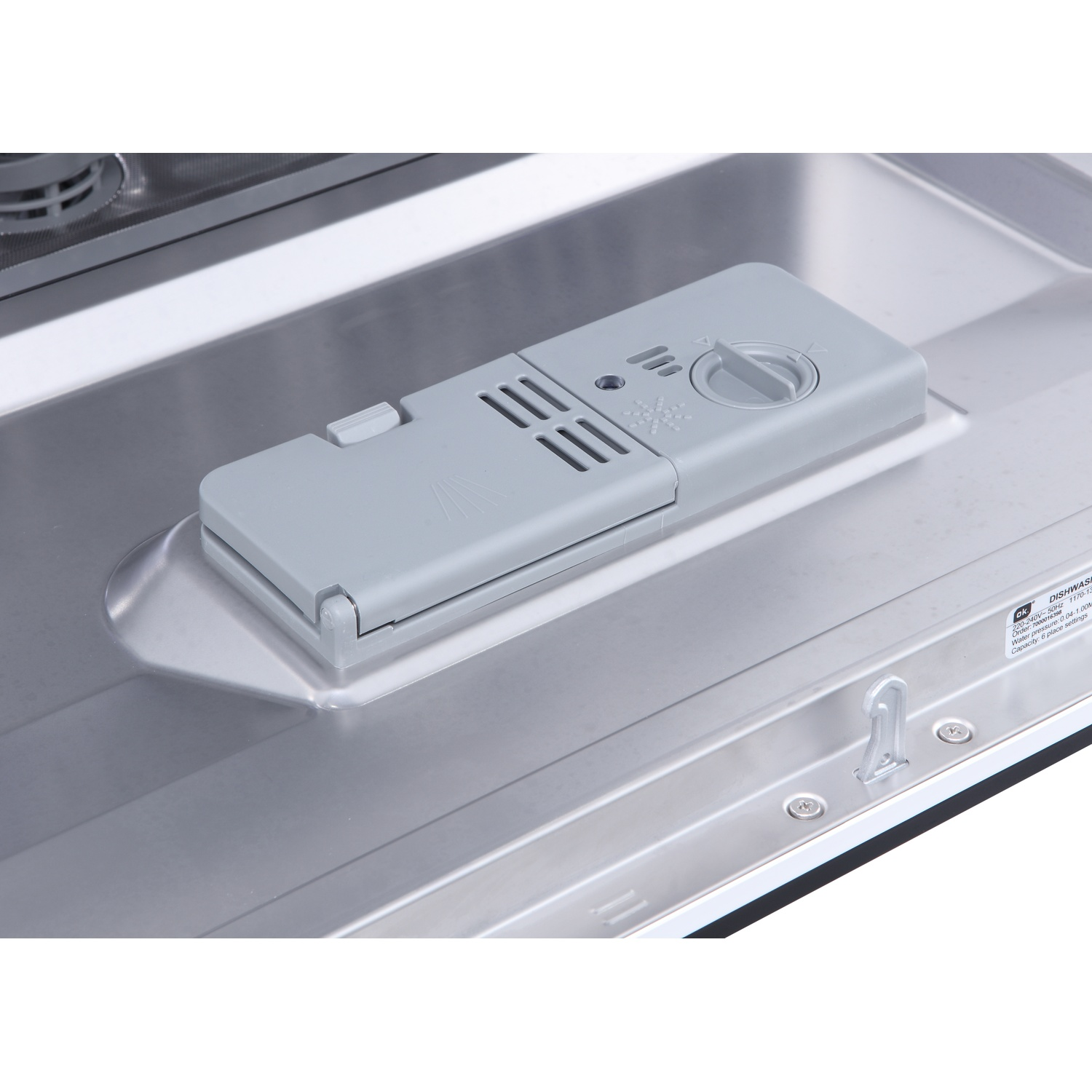 À l'intérieur d'un lave-vaisselle, un distributeur de détergent gris est ouvert, avec un cadran. Intérieur en acier inoxydable. Le distributeur est en haut.