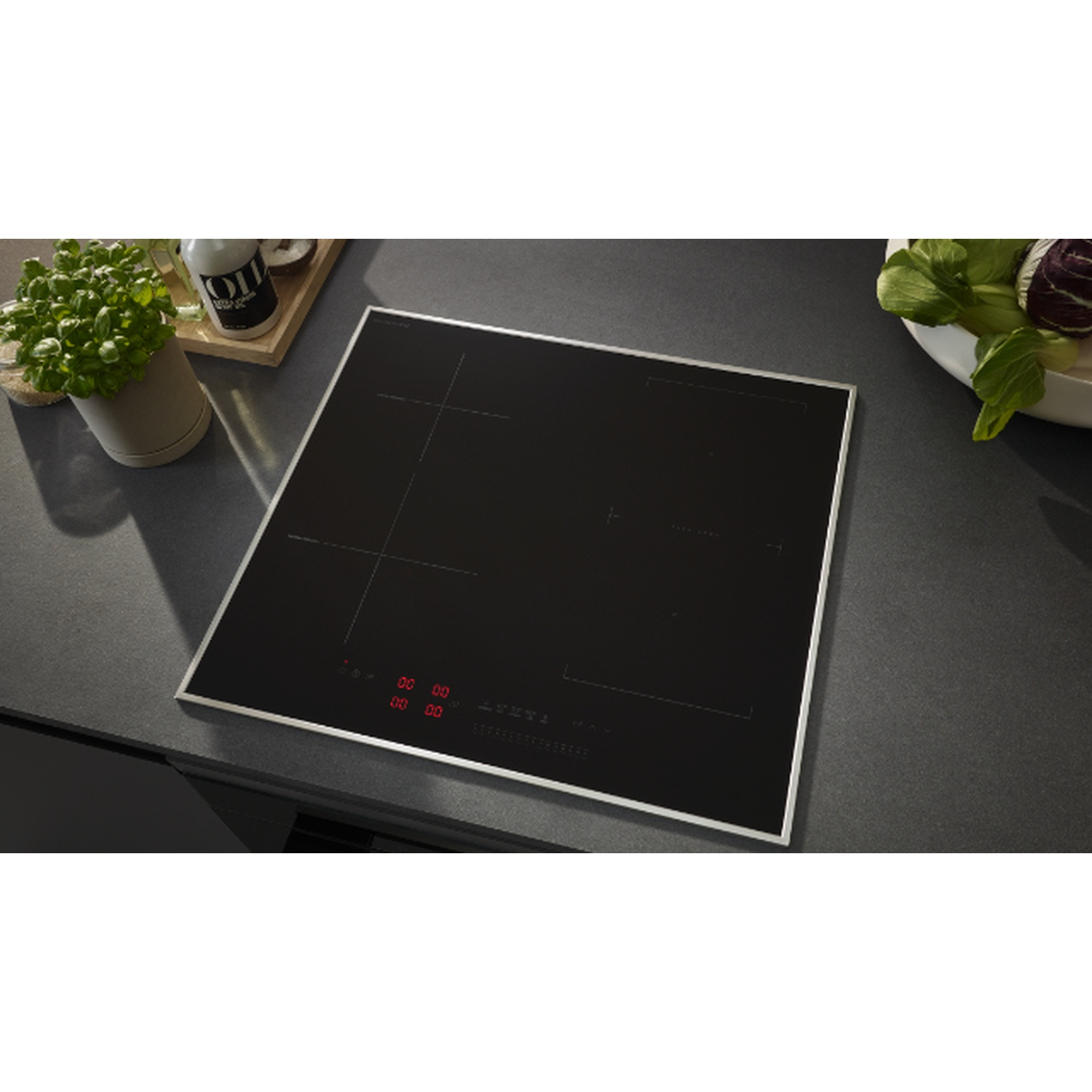 Une table de cuisson à induction noire avec des affichages numériques rouges. Une plante et une bouteille d'huile à gauche, des légumes à droite.